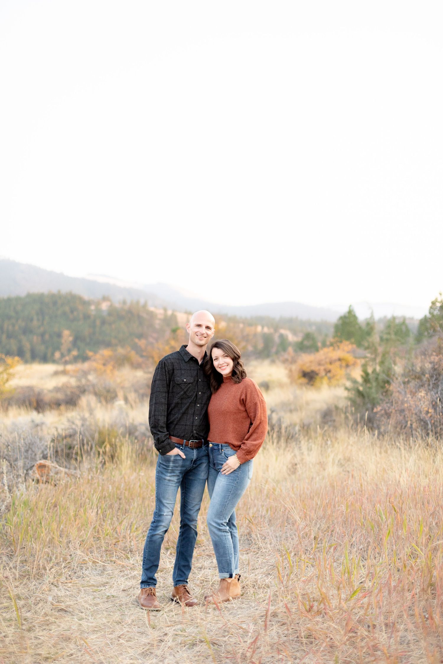 Couple standing close together smiling in an autumn mountain meadow, woman in rust sweater.