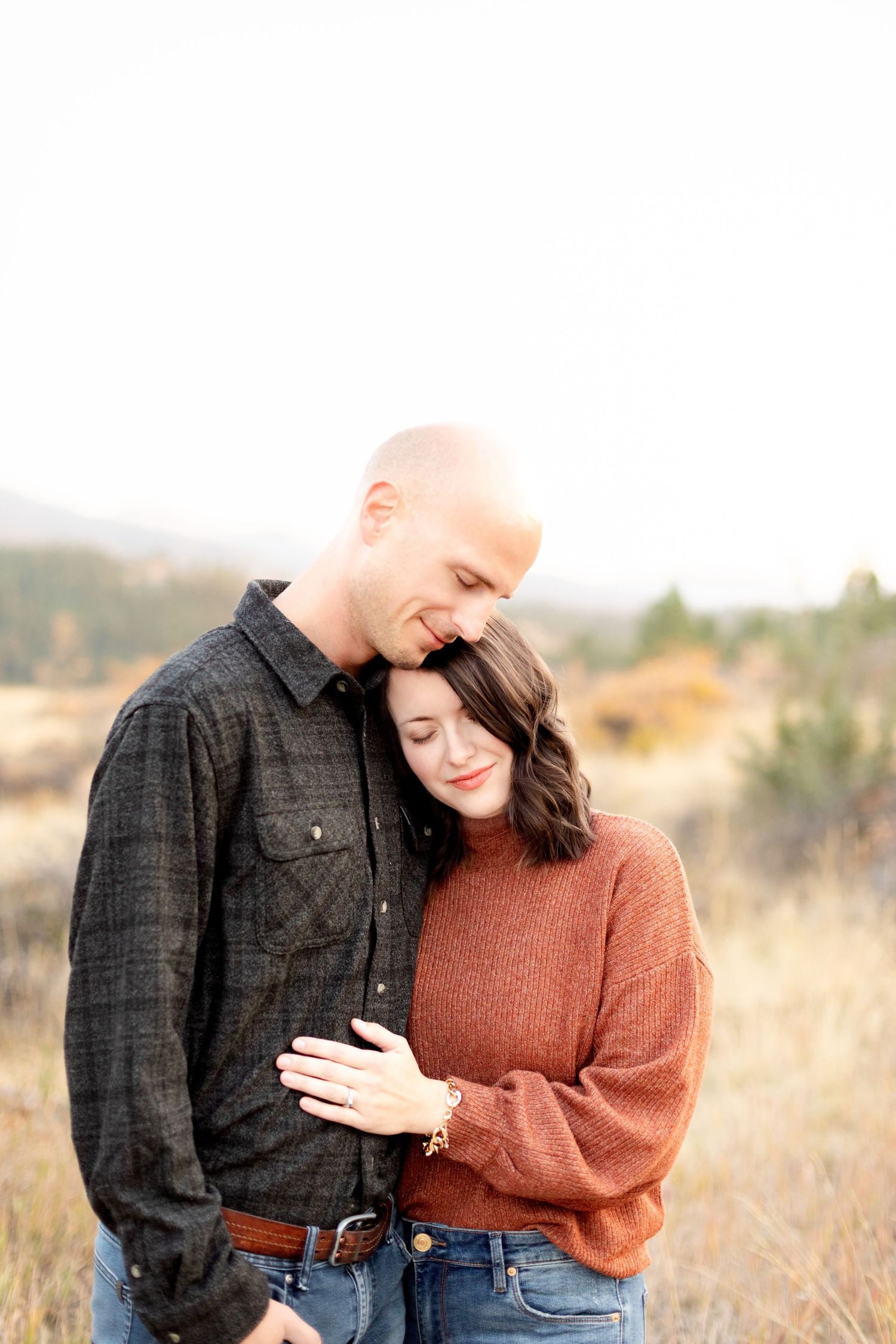 Couple sharing a tender moment in a golden field, woman resting head on mans shoulder.