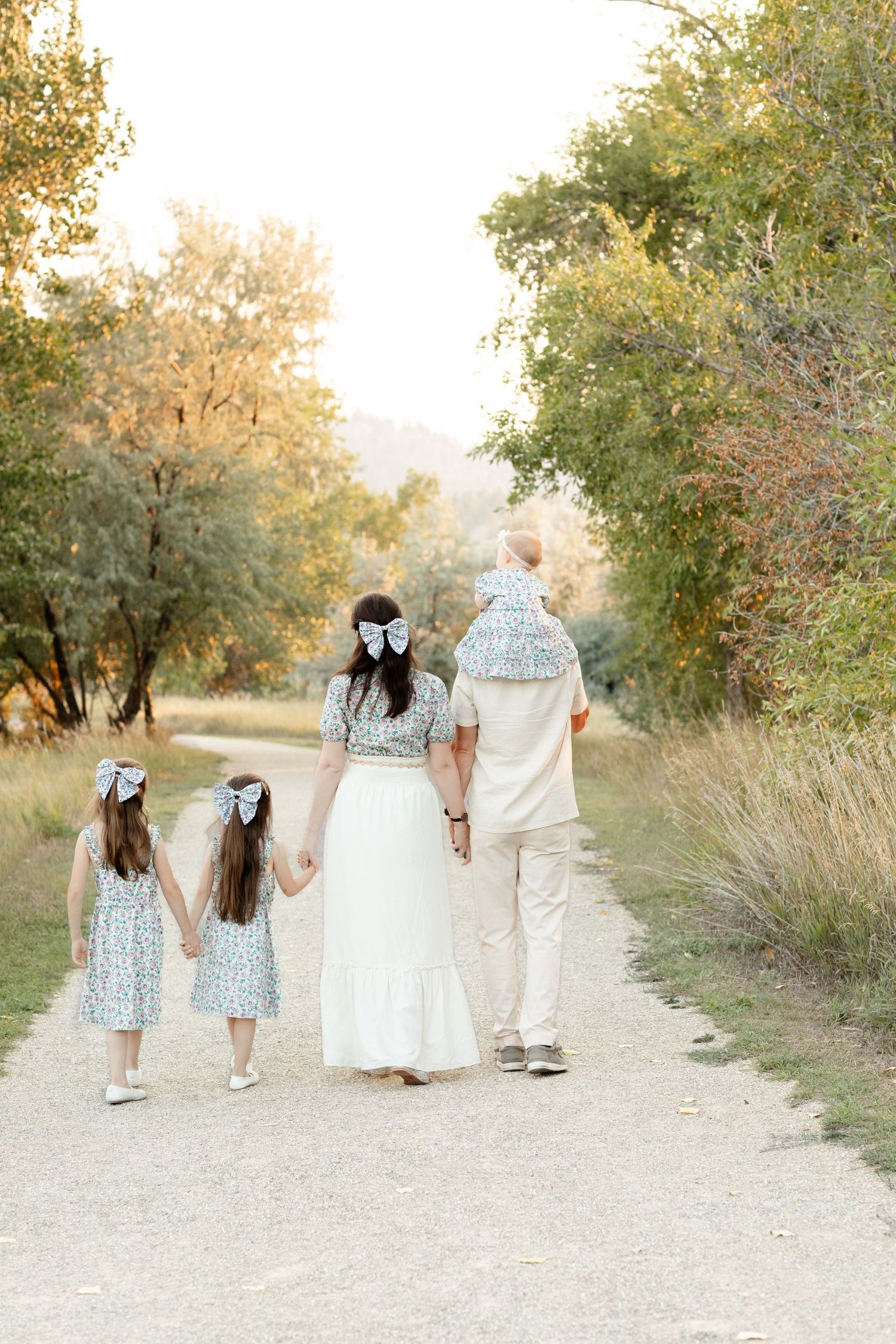 A family walks away down a tree-lined path holding hands in warm golden afternoon light.