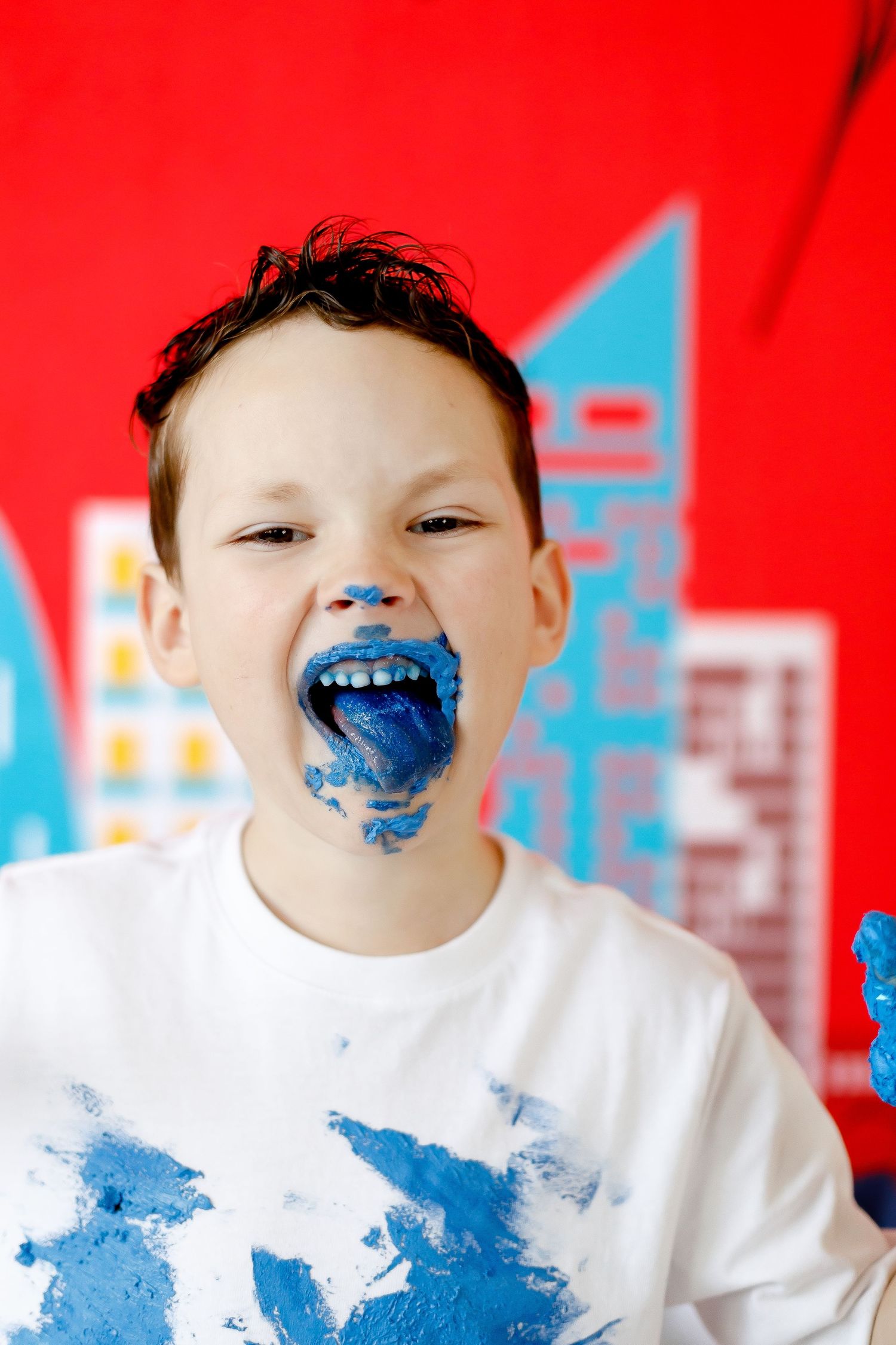 A boy with blue frosting on his face and shirt sticks out his blue-stained tongue.
