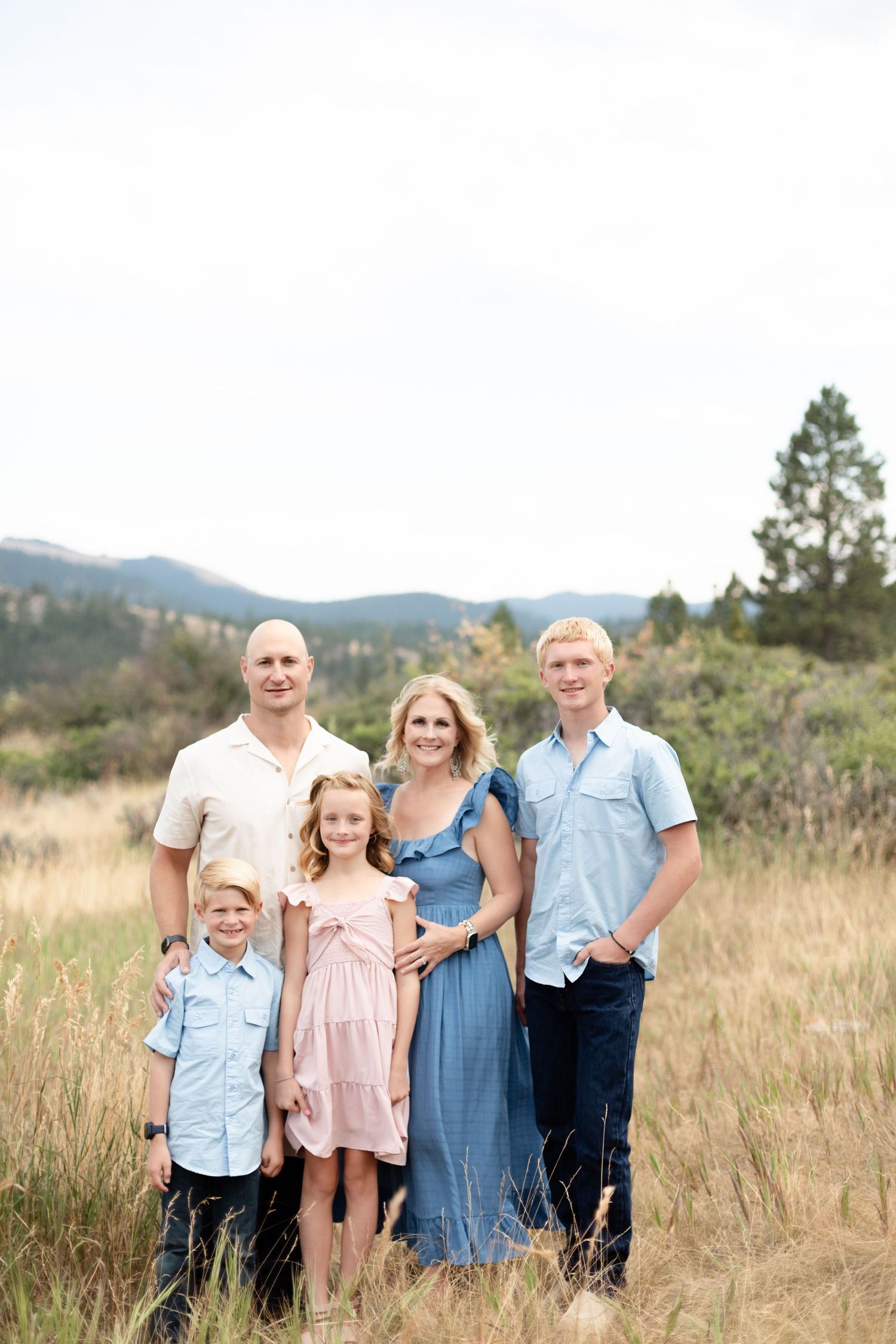 Family of five posing in a mountain meadow, parents with three children in coordinated blue and pink outfits.