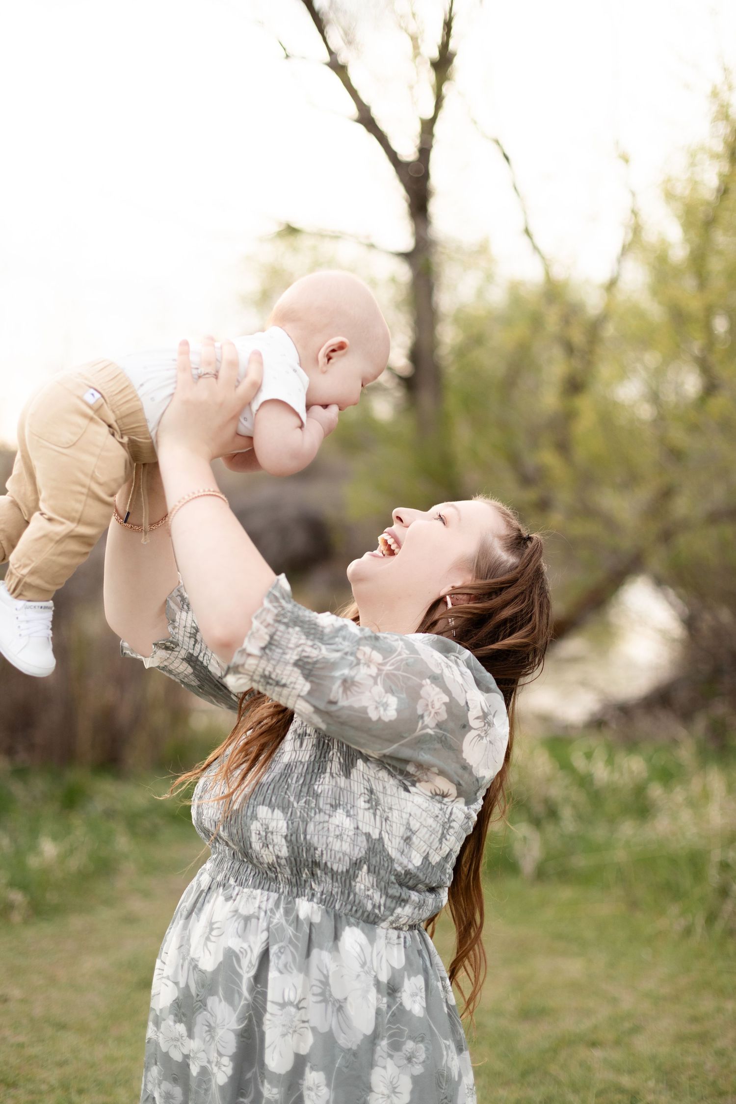 Laughing mother lifting baby up in the air during outdoor spring family photo session.