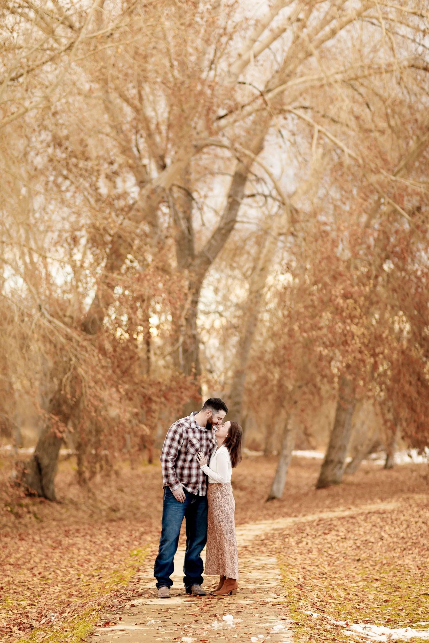 Couple sharing a kiss on a scenic autumn path lined with golden leaf-covered trees.