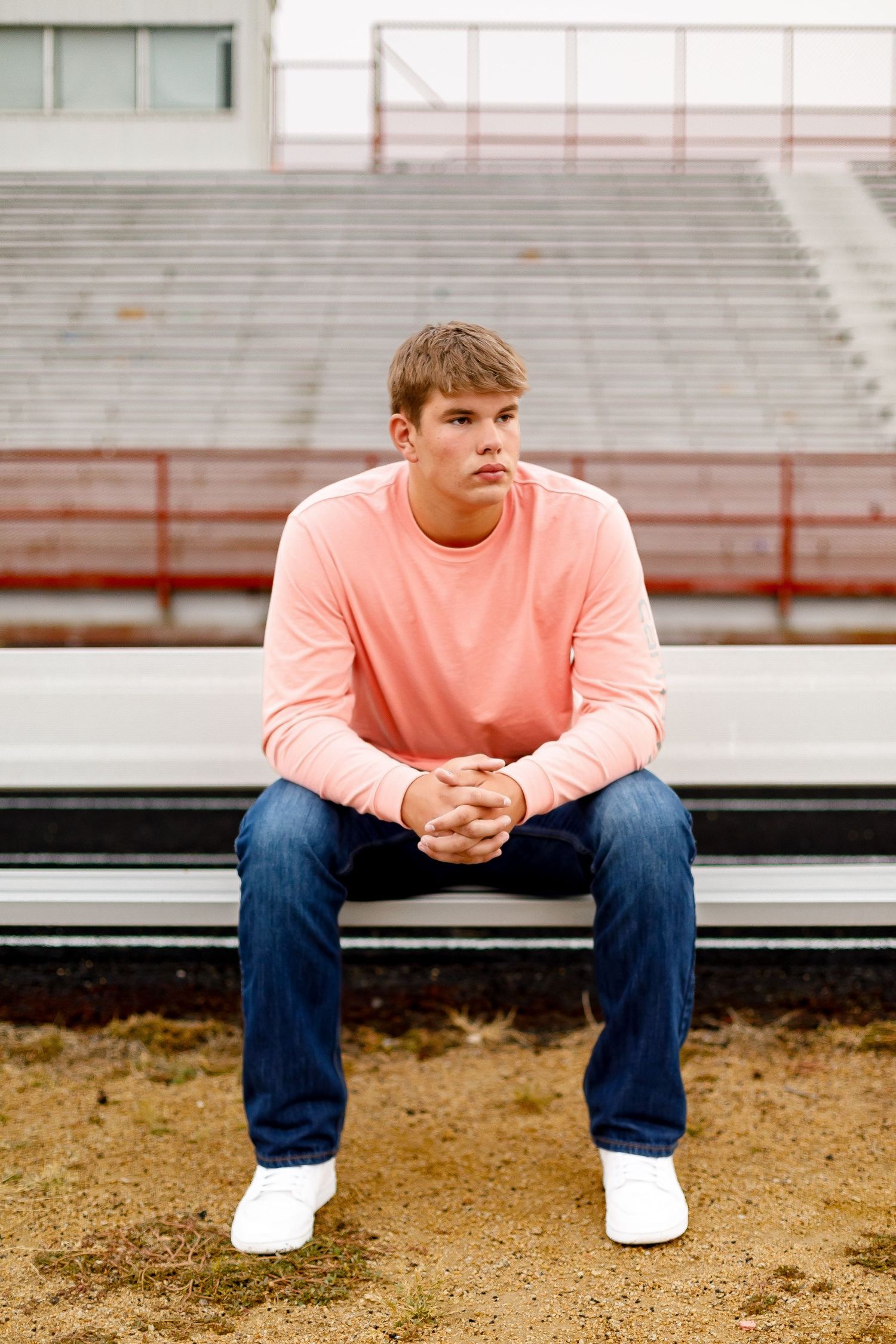 Teen in pink long-sleeve shirt and jeans sitting on bleachers with hands clasped looking sideways.