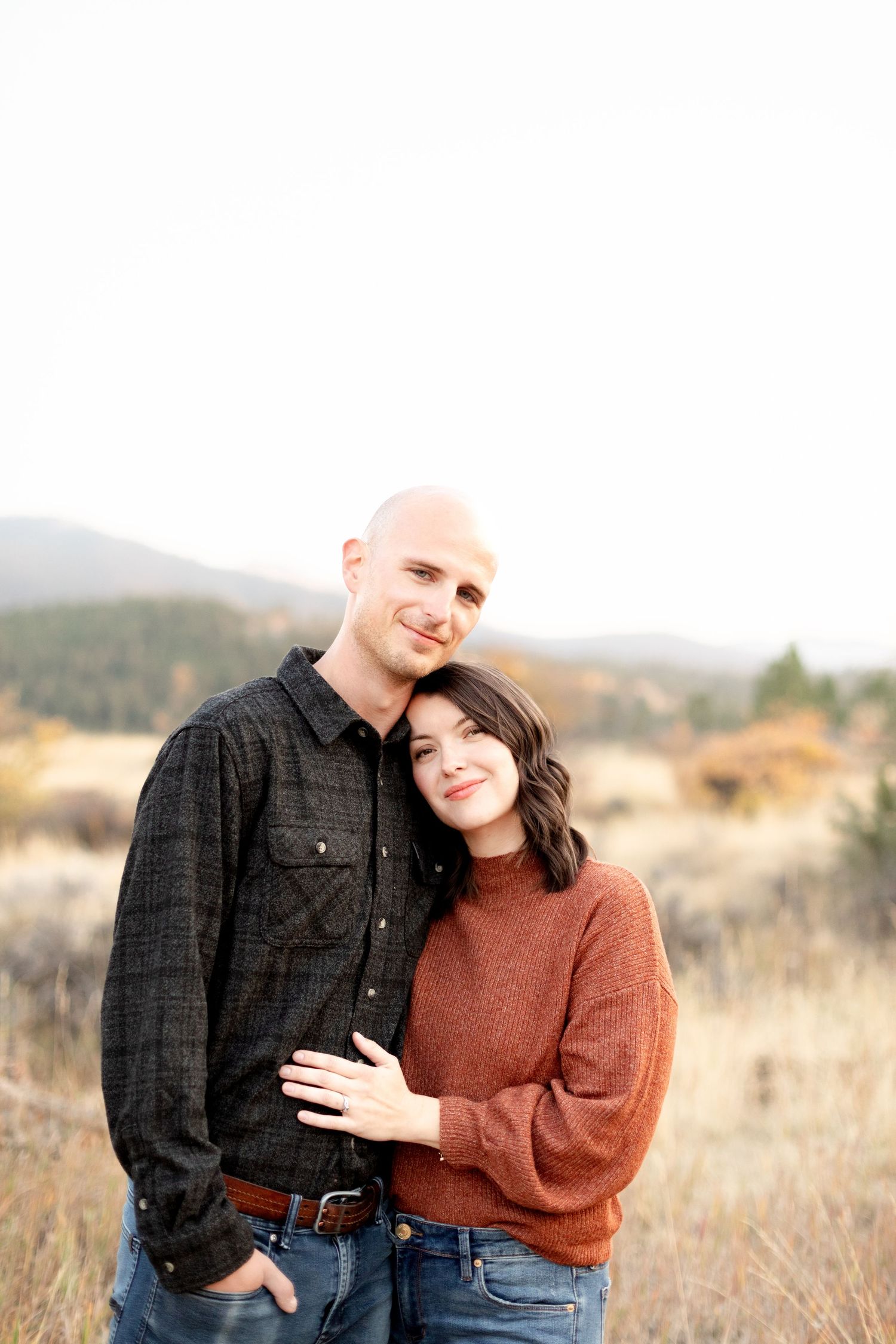 Couple embracing and smiling in an autumn mountain meadow, woman in rust sweater and jeans.