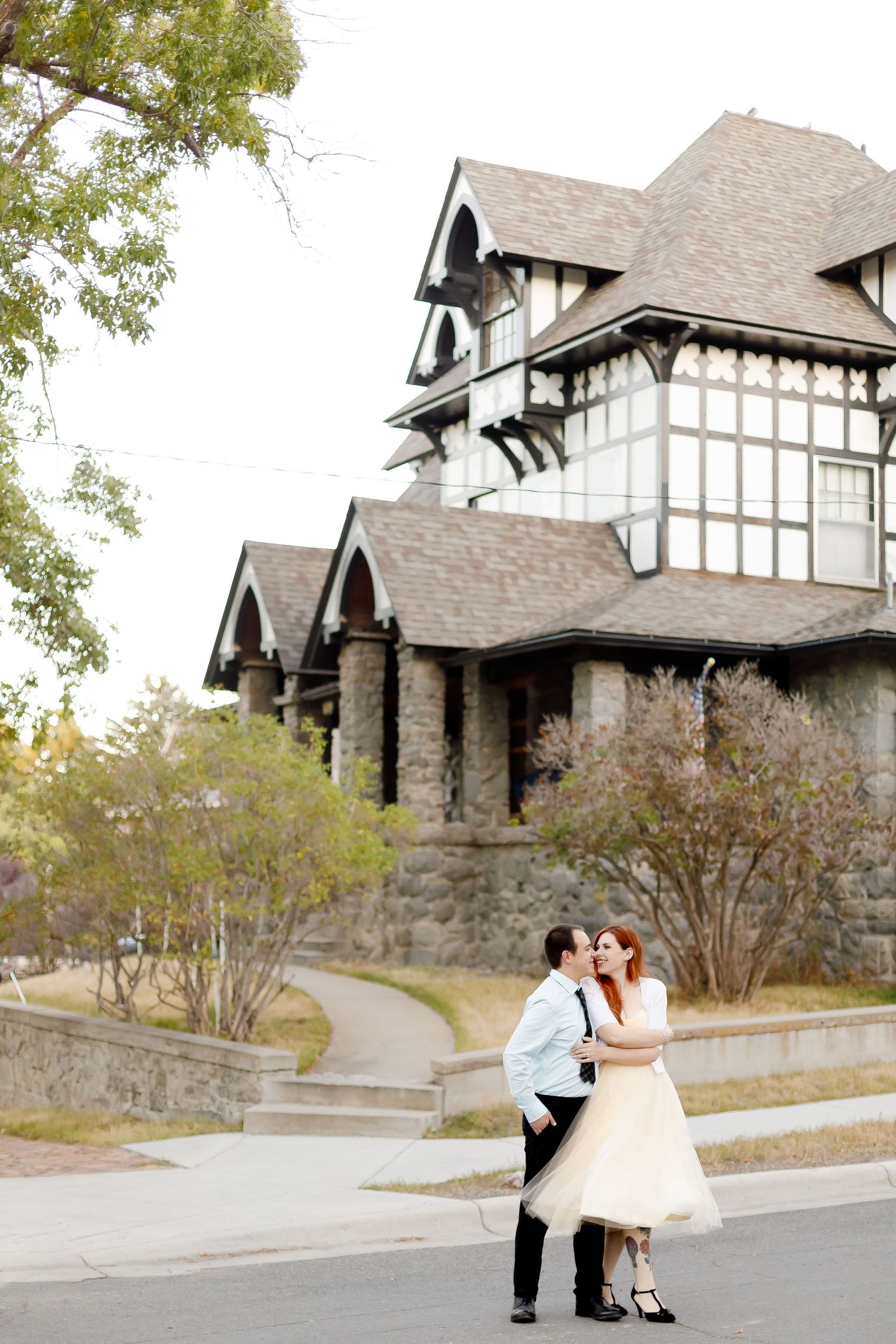 Bride and groom kissing on a street in front of a historic Tudor-style building.