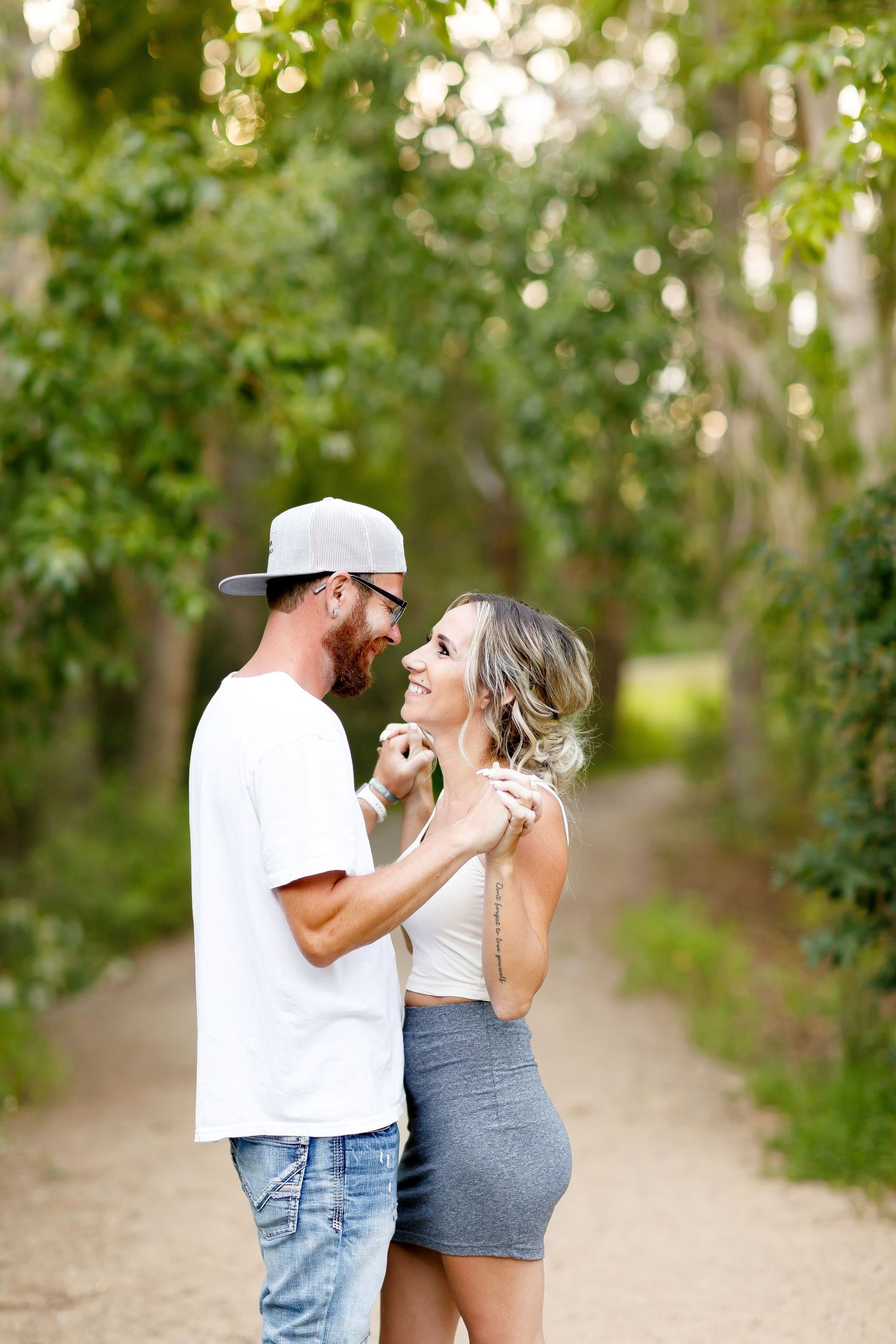 Happy couple gazing at each other and laughing on a lush green tree-lined pathway.