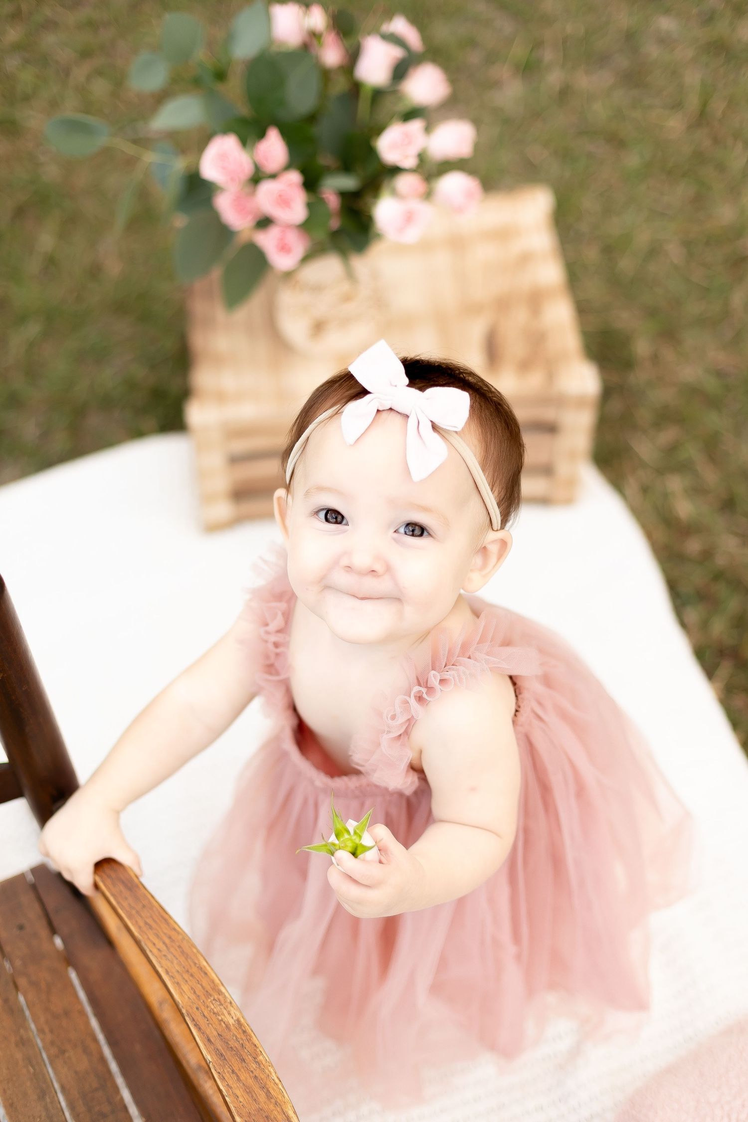 Adorable baby girl in pink tutu dress and bow headband smiling during outdoor photo session.