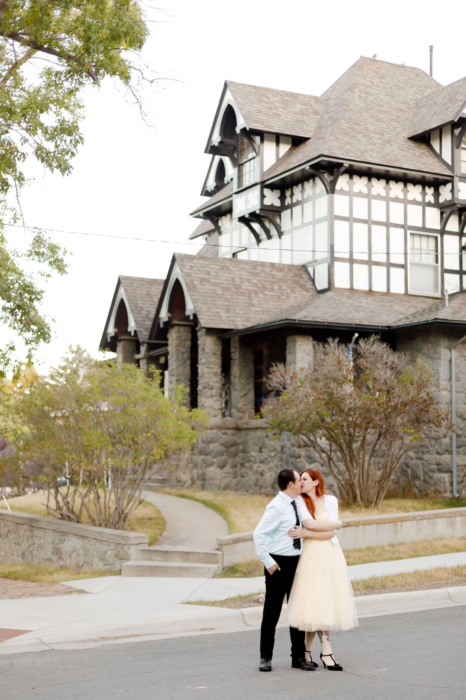 Bride and groom embracing and kissing outside a grand historic Tudor-style stone building.