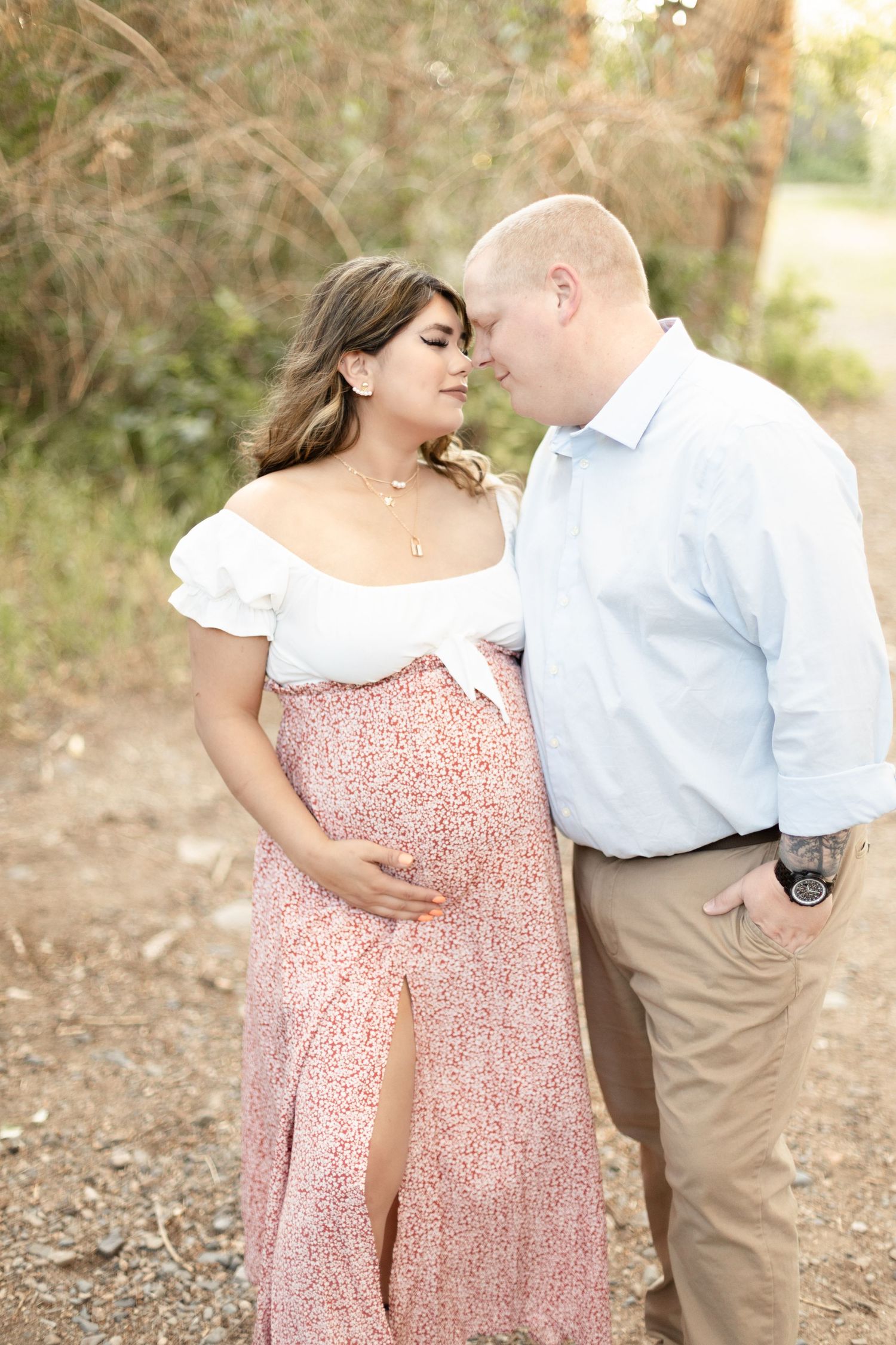 Expectant couple sharing an intimate forehead touch on a wooded path during a romantic outdoor maternity photo session.