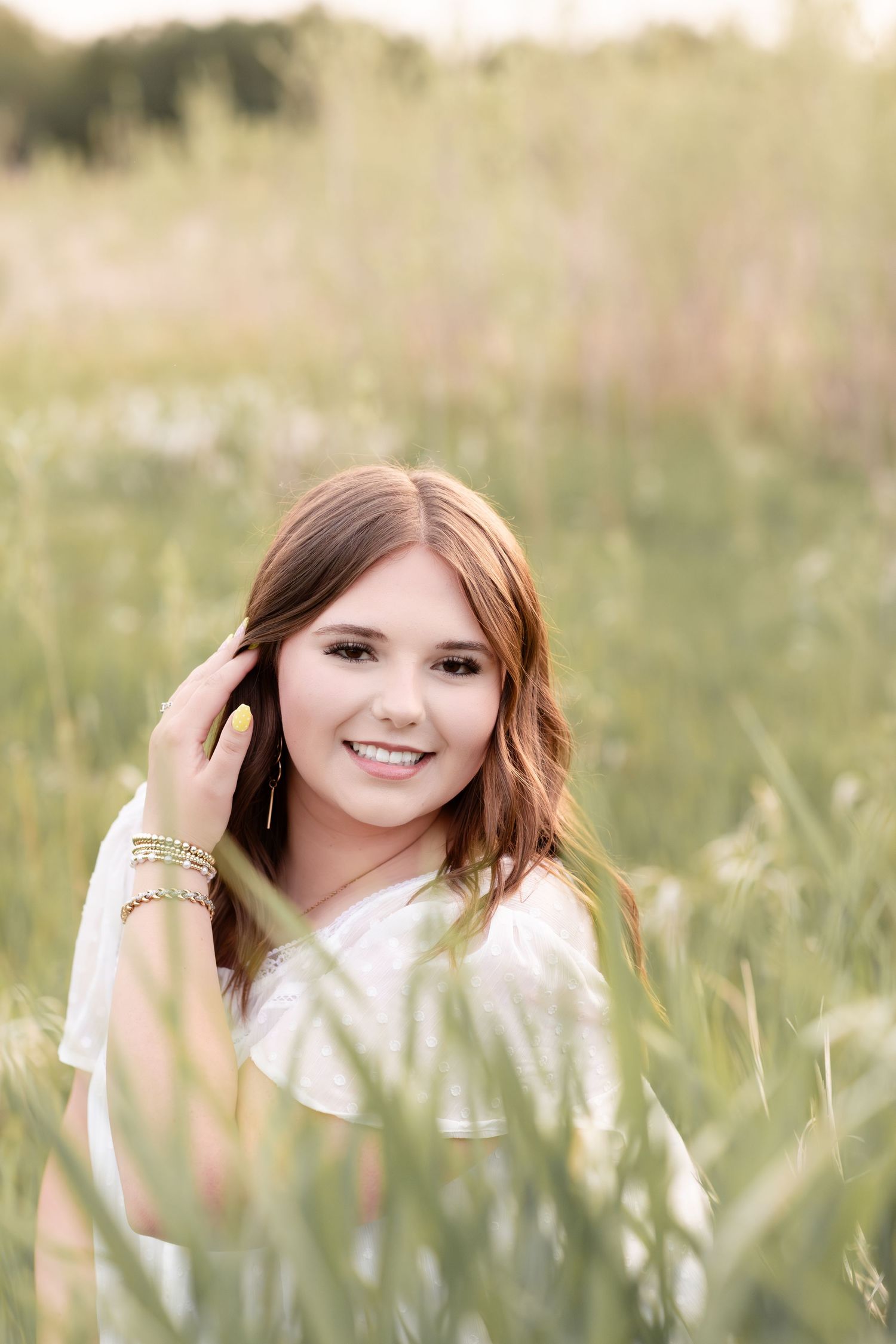 Smiling teenage girl with auburn hair posing in sunlit tall grass meadow outdoors.