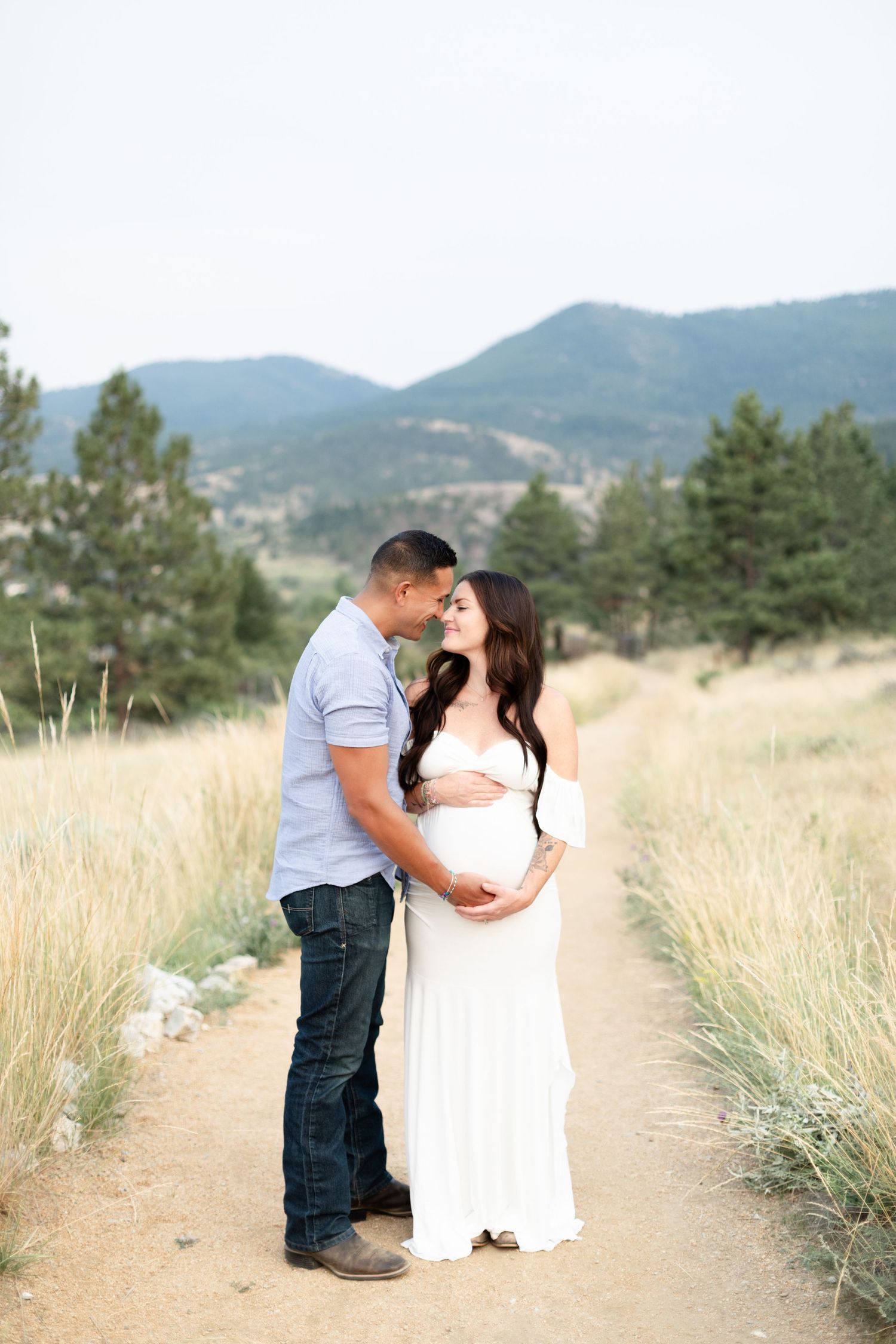 Expecting couple embracing on dirt path surrounded by golden grass and mountains.