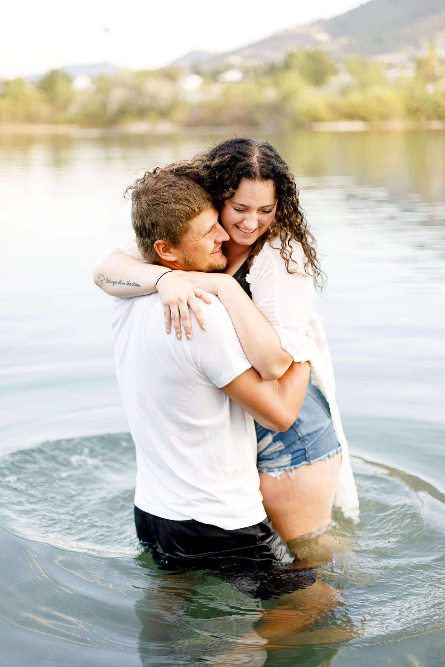 Happy couple hugging and laughing together while standing in a lake with mountain scenery.