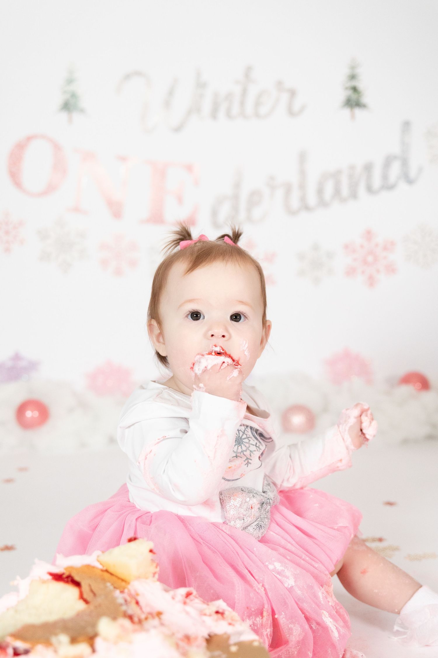 Baby girl in pink tutu eating cake at Winter ONEderland first birthday cake smash session.