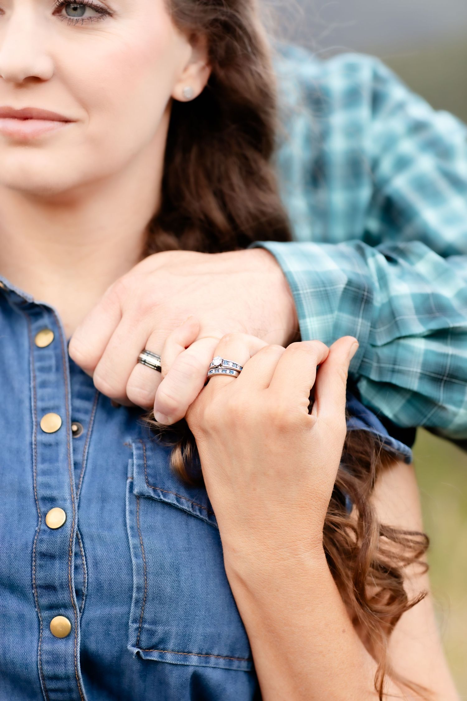 Close-up of a couple holding hands showing wedding and engagement rings in an outdoor setting.