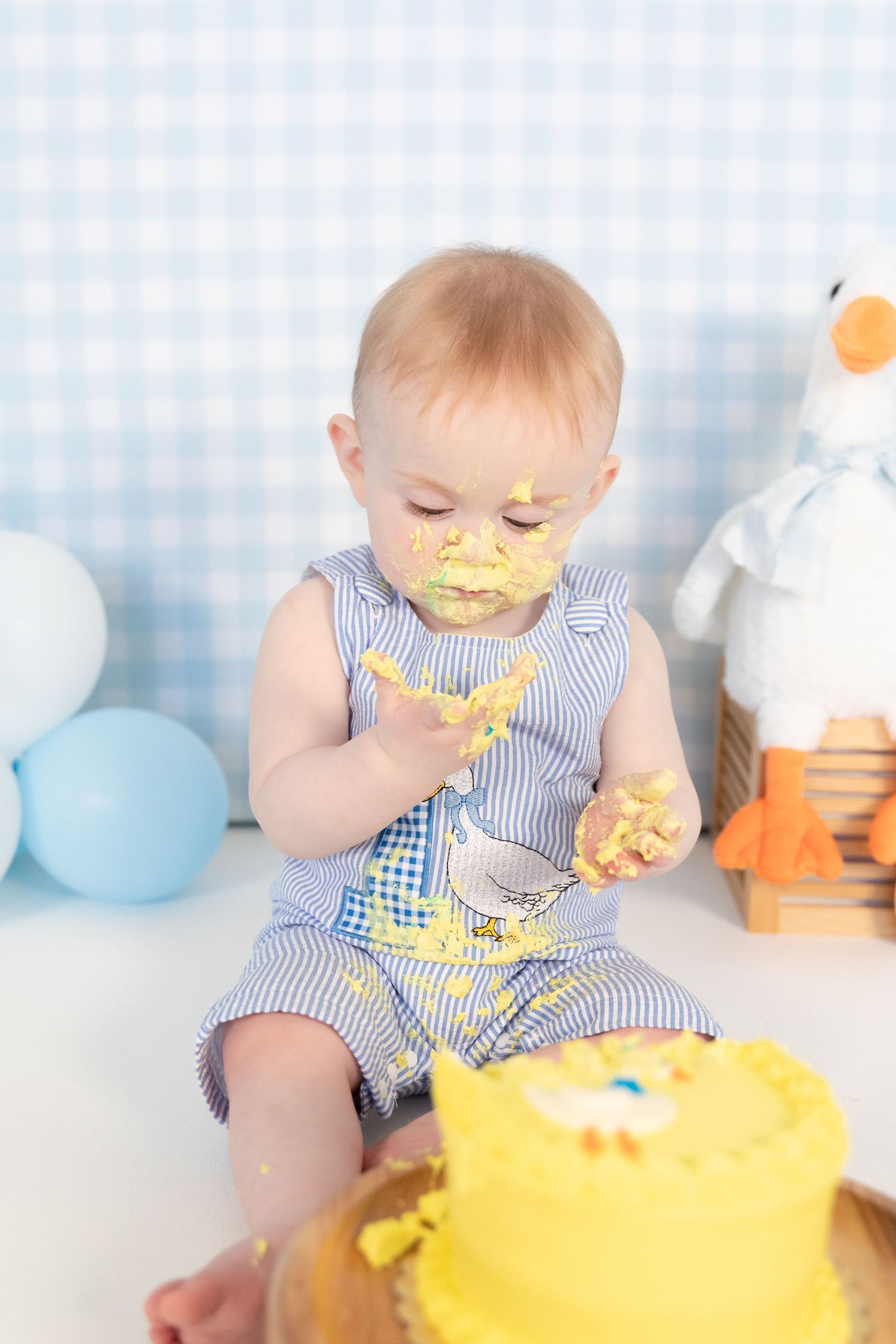 Messy baby in blue striped outfit smashing yellow birthday cake during first birthday celebration.