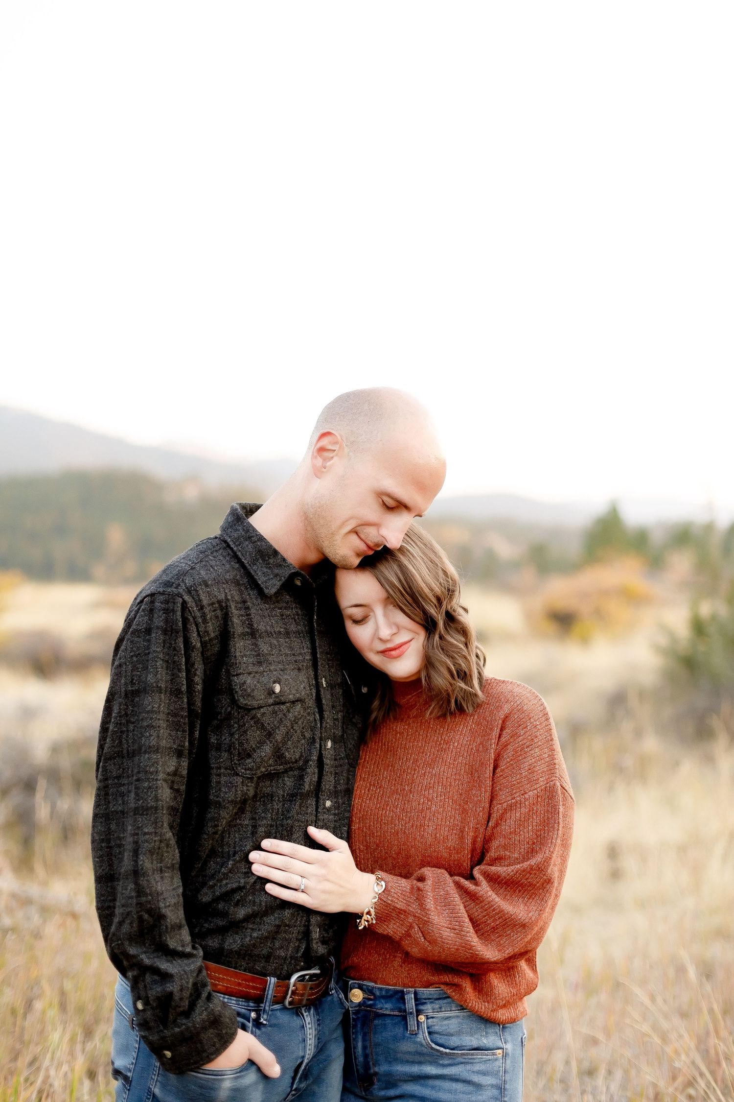 Couple embracing tenderly in an autumn meadow with mountains and golden grass in the background.
