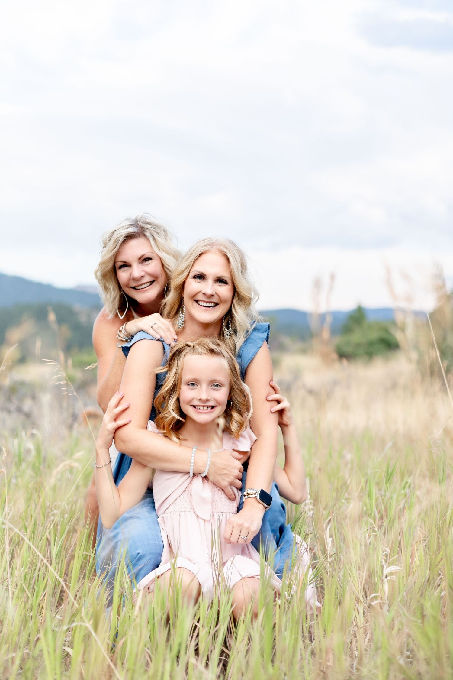Three generations of women, grandmother, mother, and granddaughter, posing in a tall grass field.