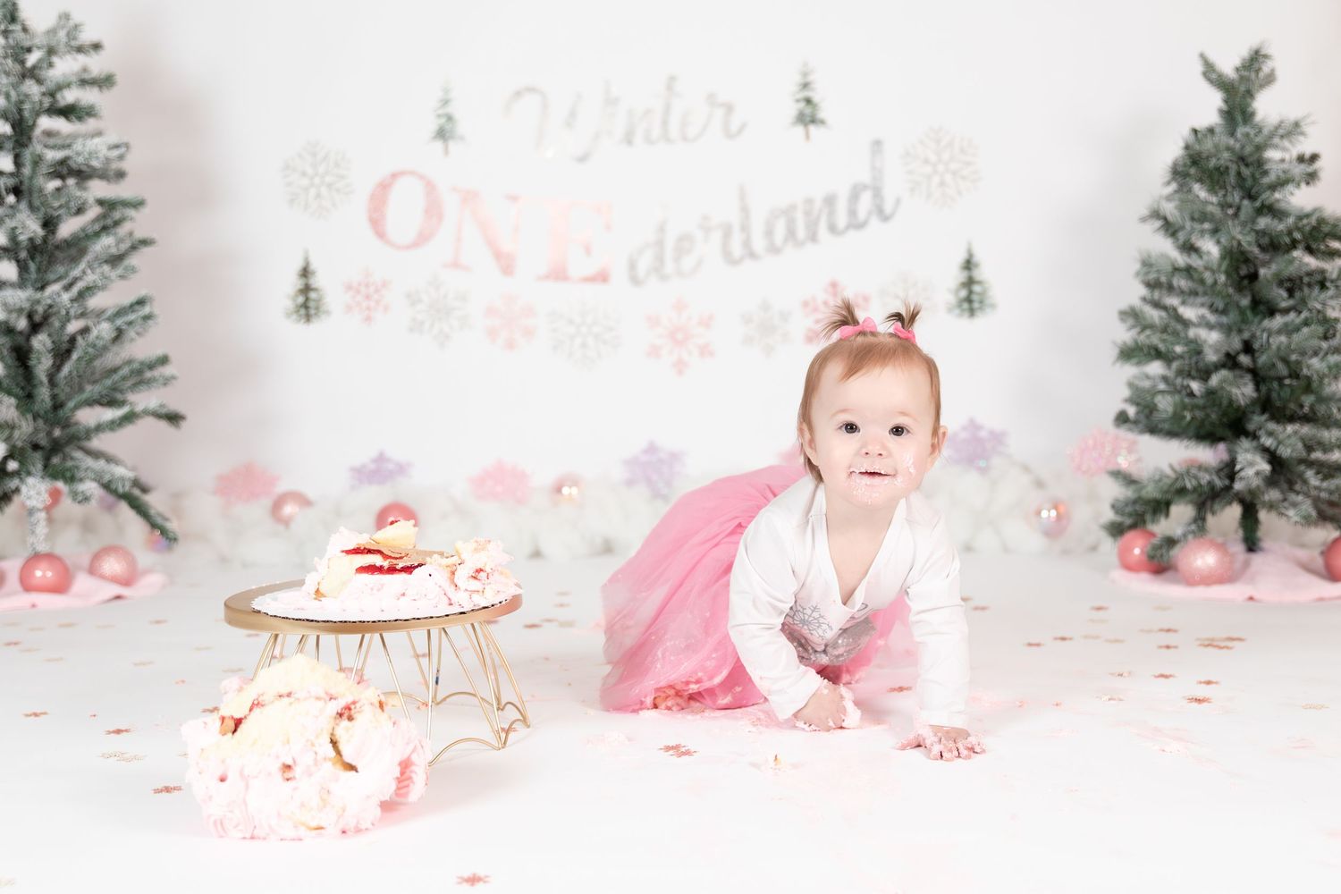 Baby girl in pink dress crawling toward smash cake at Winter ONEderland first birthday photo session.
