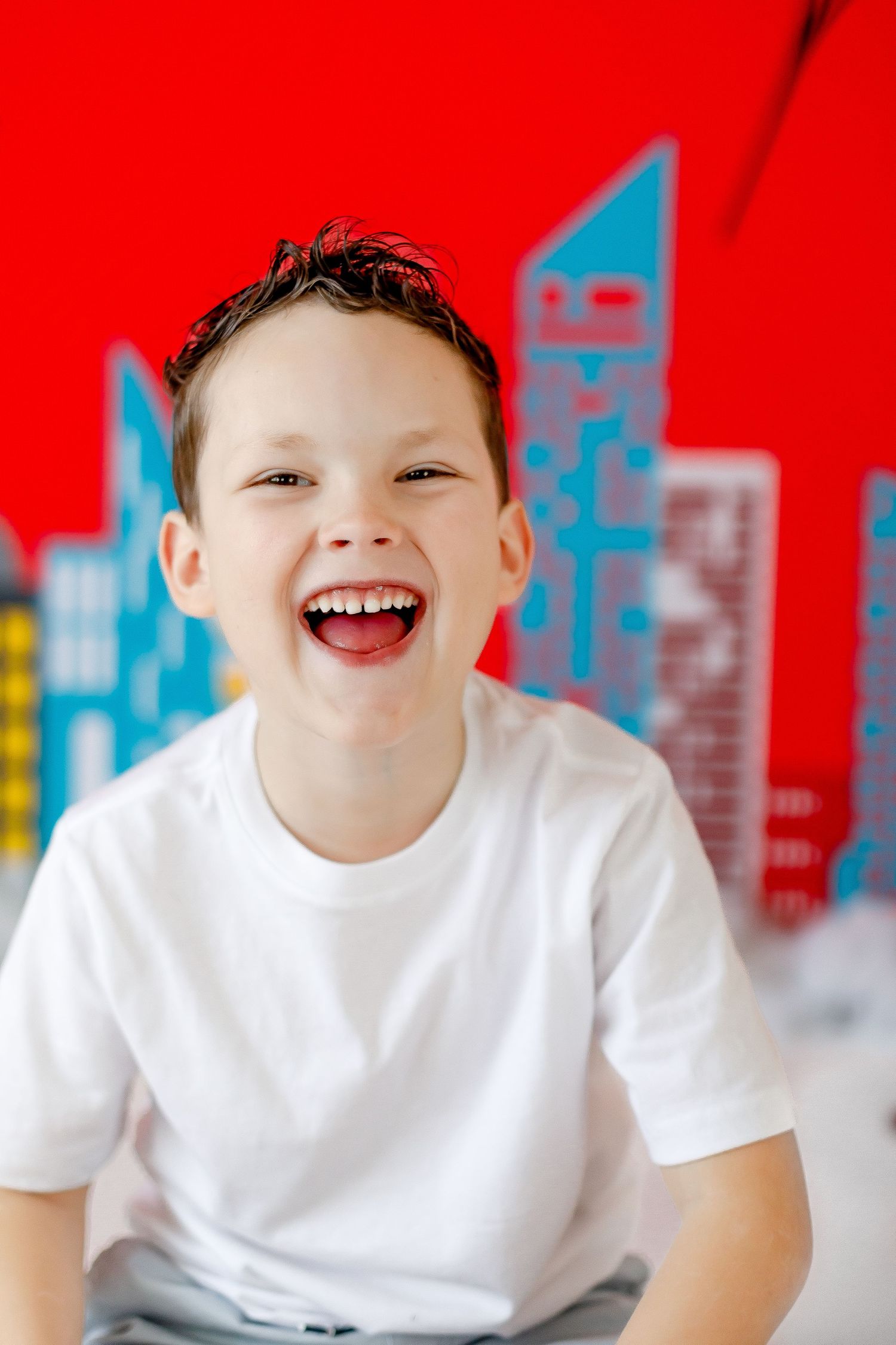 A laughing boy in a white t-shirt poses in front of a red Spider-Man cityscape birthday backdrop.