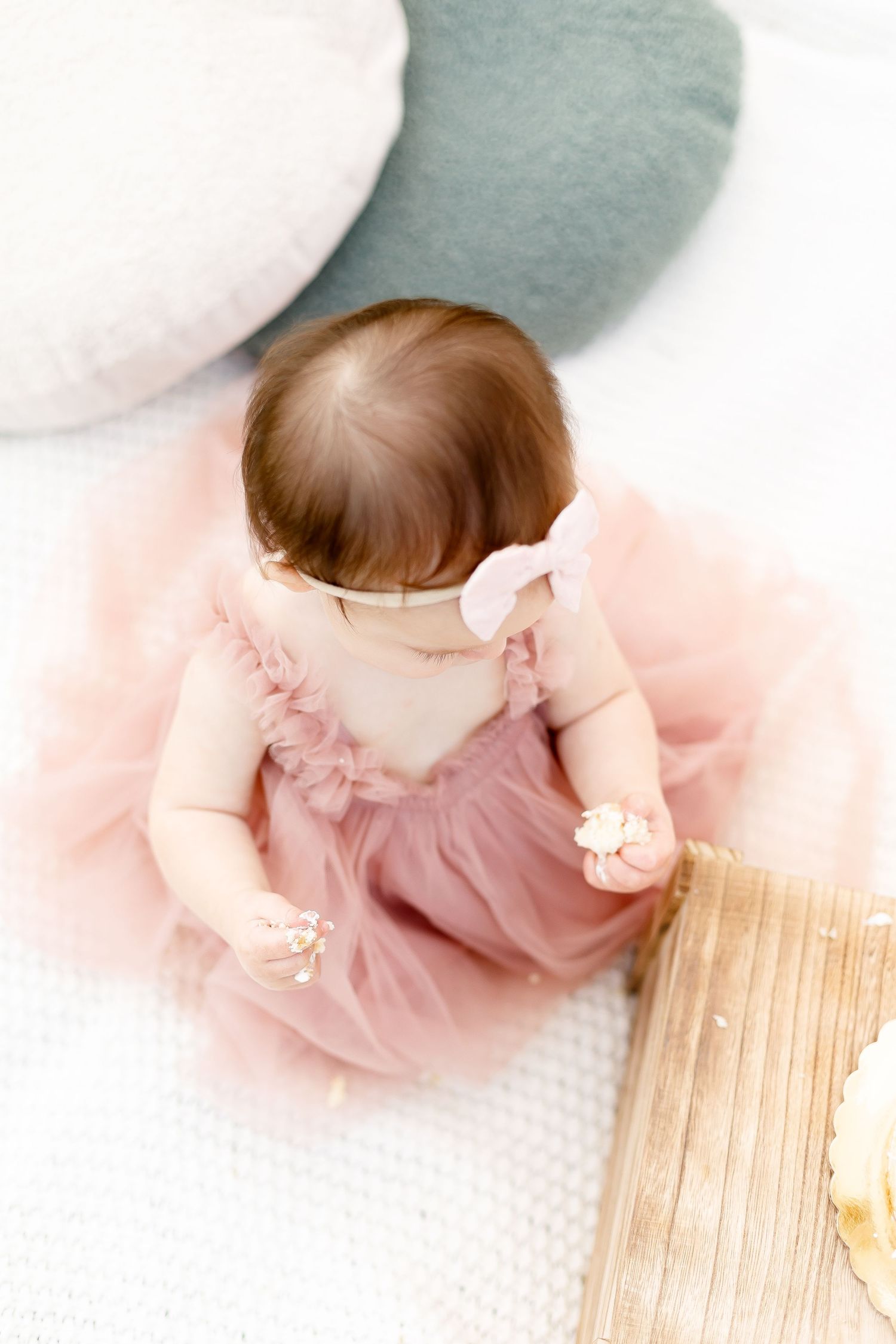 Baby girl in pink tulle dress viewed from above sitting on white blanket at birthday photo session.