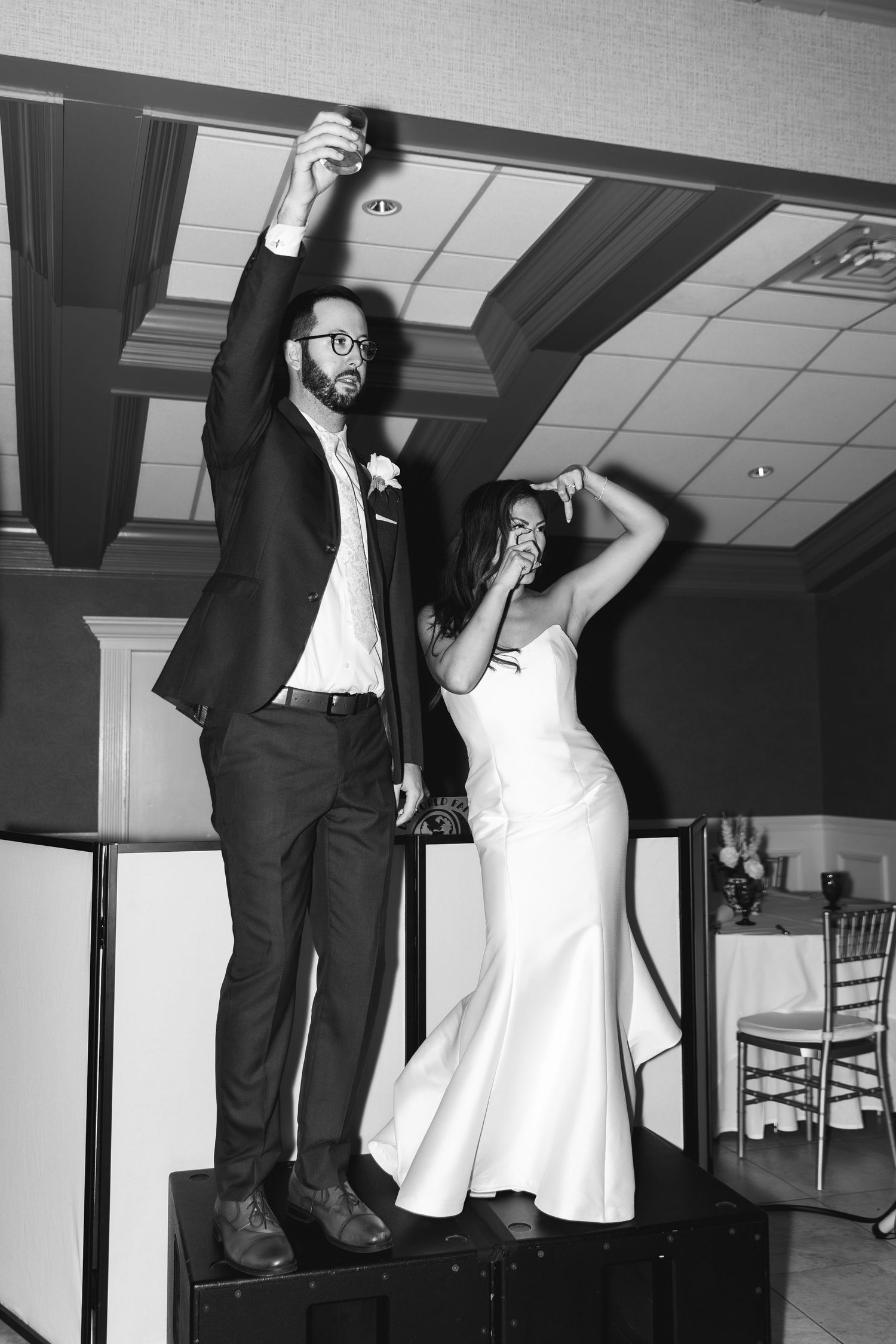 Black and white photo of a bride and groom celebrating on a stage at their wedding reception.