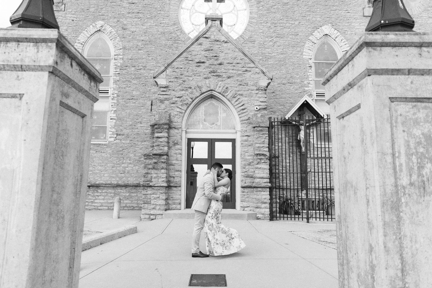 Black and white photo of a couple sharing a romantic kiss outside a historic stone church on their wedding day.
