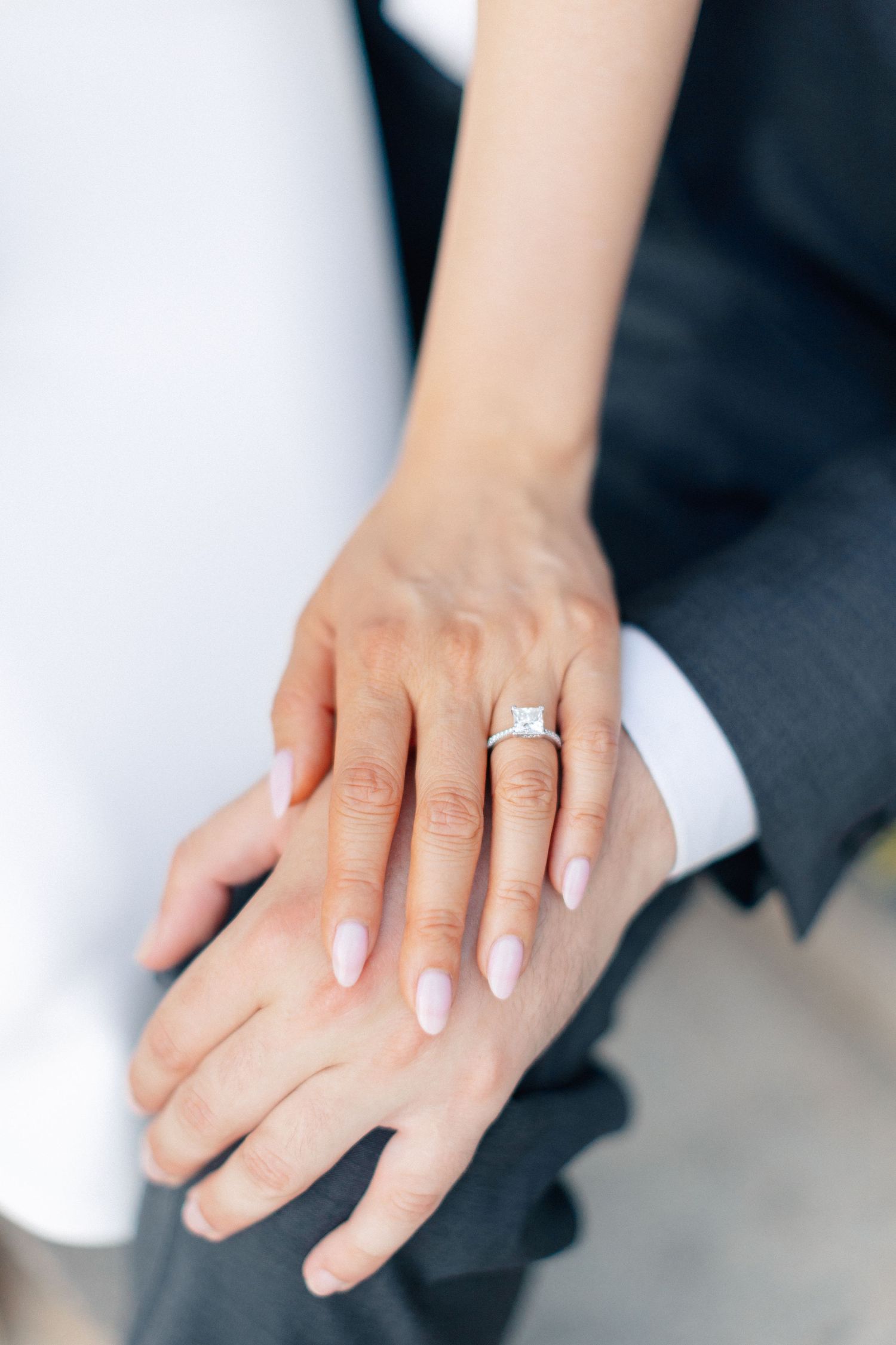 Close-up of bride and groom hands showing elegant square diamond engagement ring with pink manicure.