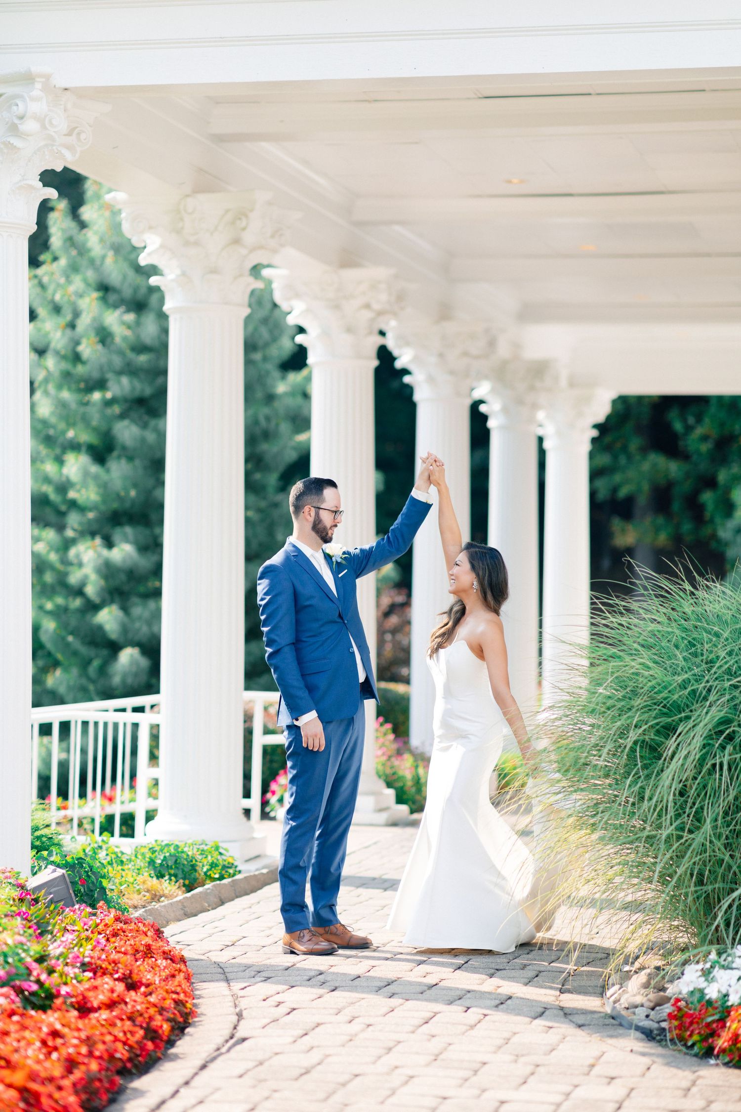 Bride and groom dancing under white columns surrounded by colorful flowers at an elegant outdoor wedding venue.