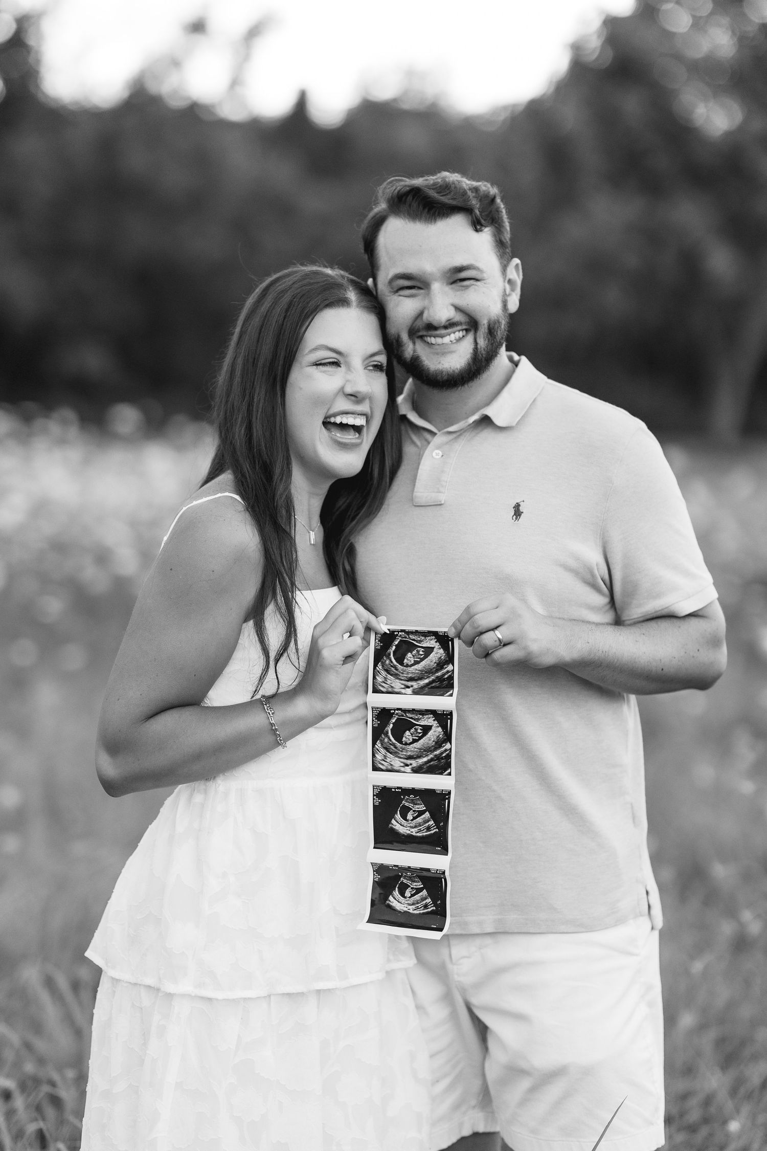 Joyful couple laughing and holding ultrasound photos in black and white outdoor portrait in Ohio portrait session.