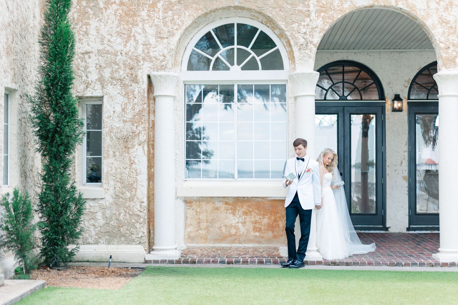 Elegant bride and groom posing outside a grand venue with white columns and arched windows on their wedding day, wedding at Bella Cosa
