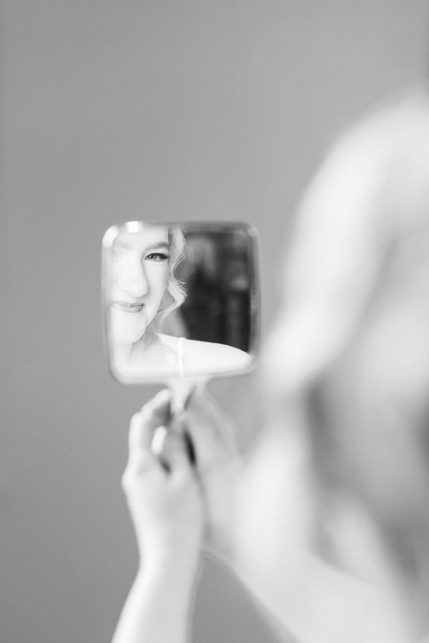 Black and white photo of a smiling woman reflected in a small handheld mirror.