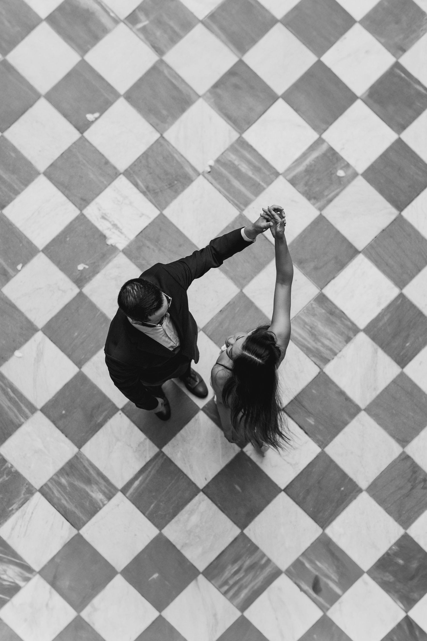 Black and white overhead view of a couple dancing together on a classic checkered marble floor.