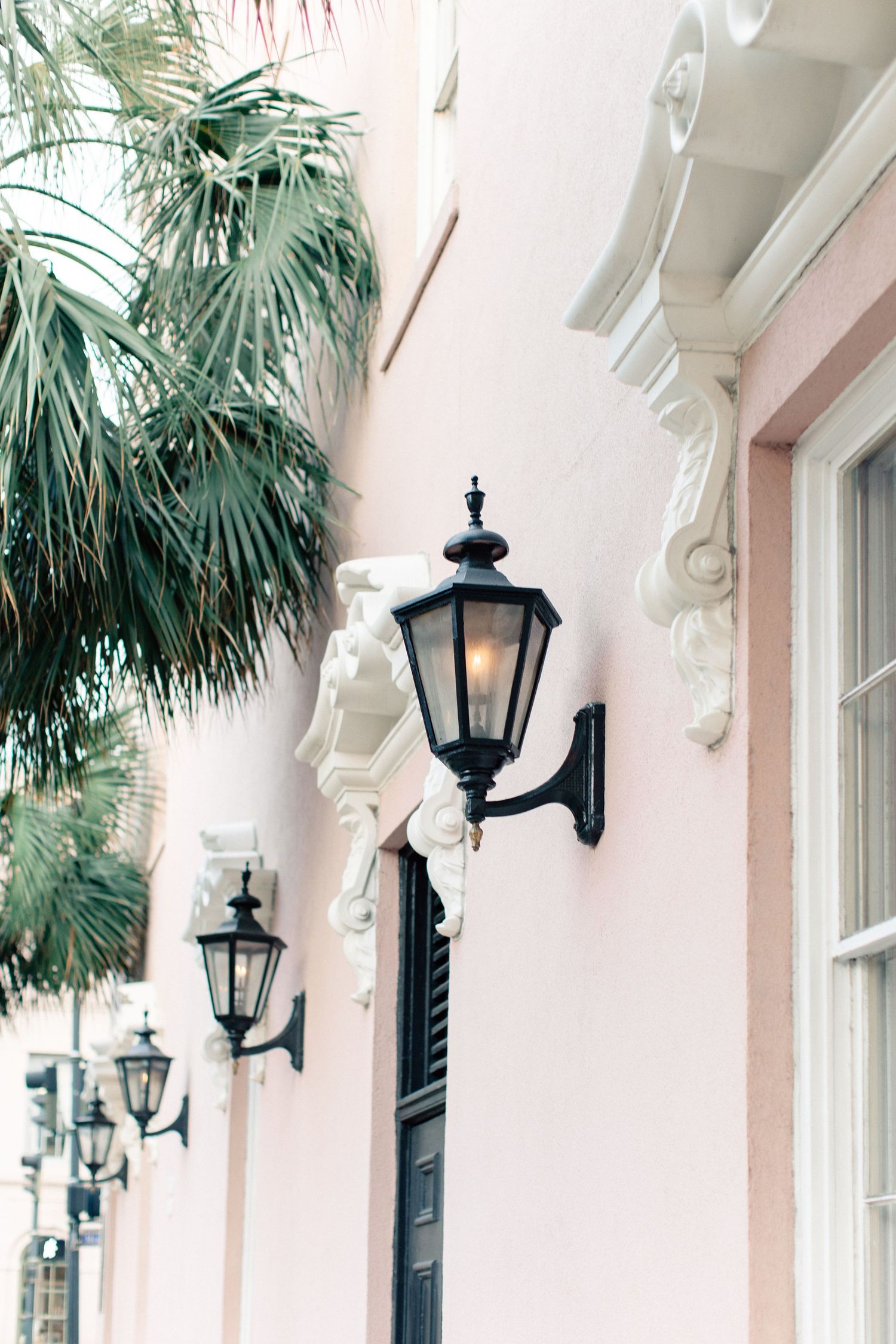 Row of elegant black iron lanterns on a pink historic building facade with ornate white moldings.