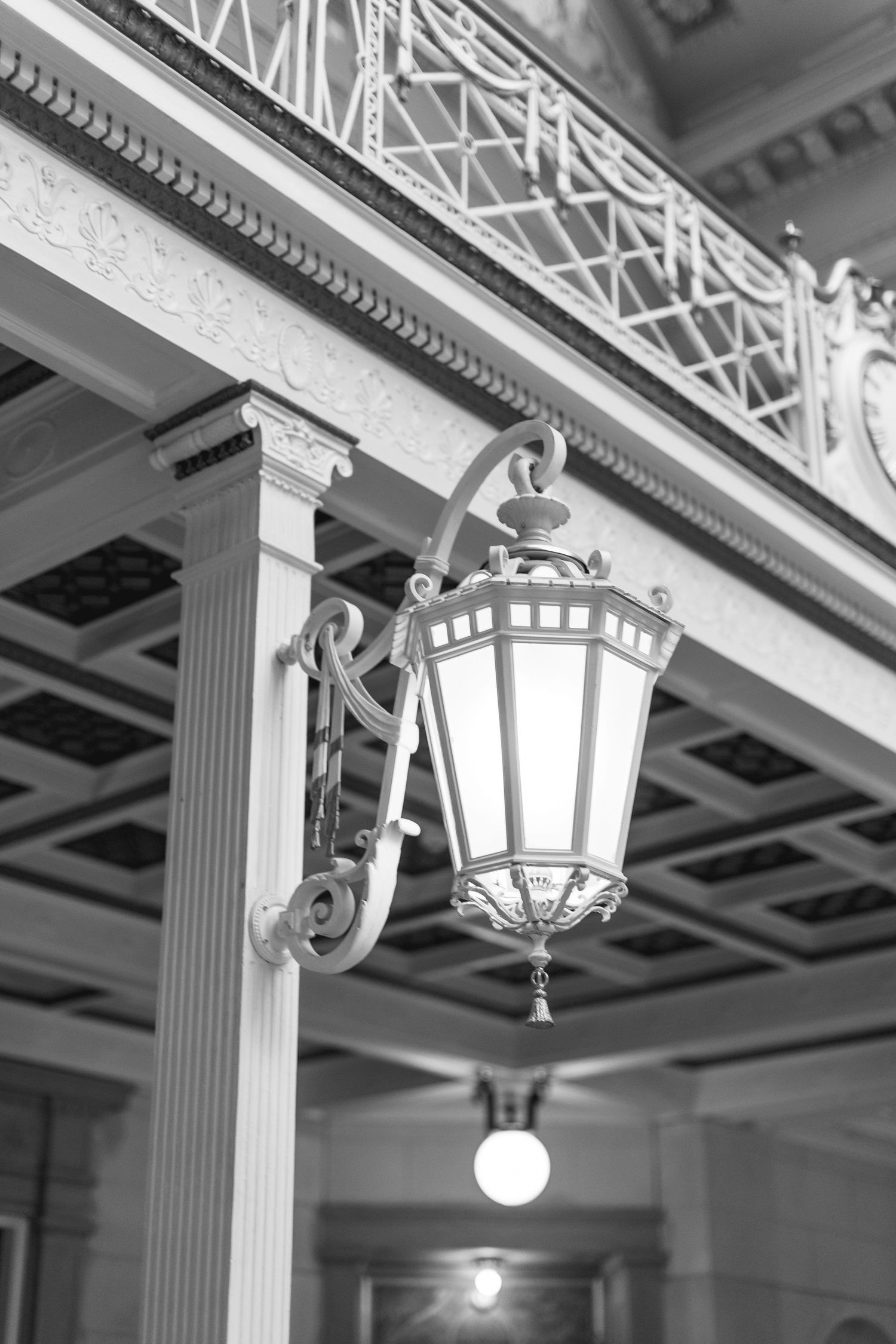 Ornate vintage wall lantern mounted on a classical column in an elegant interior hallway with decorative ceiling.