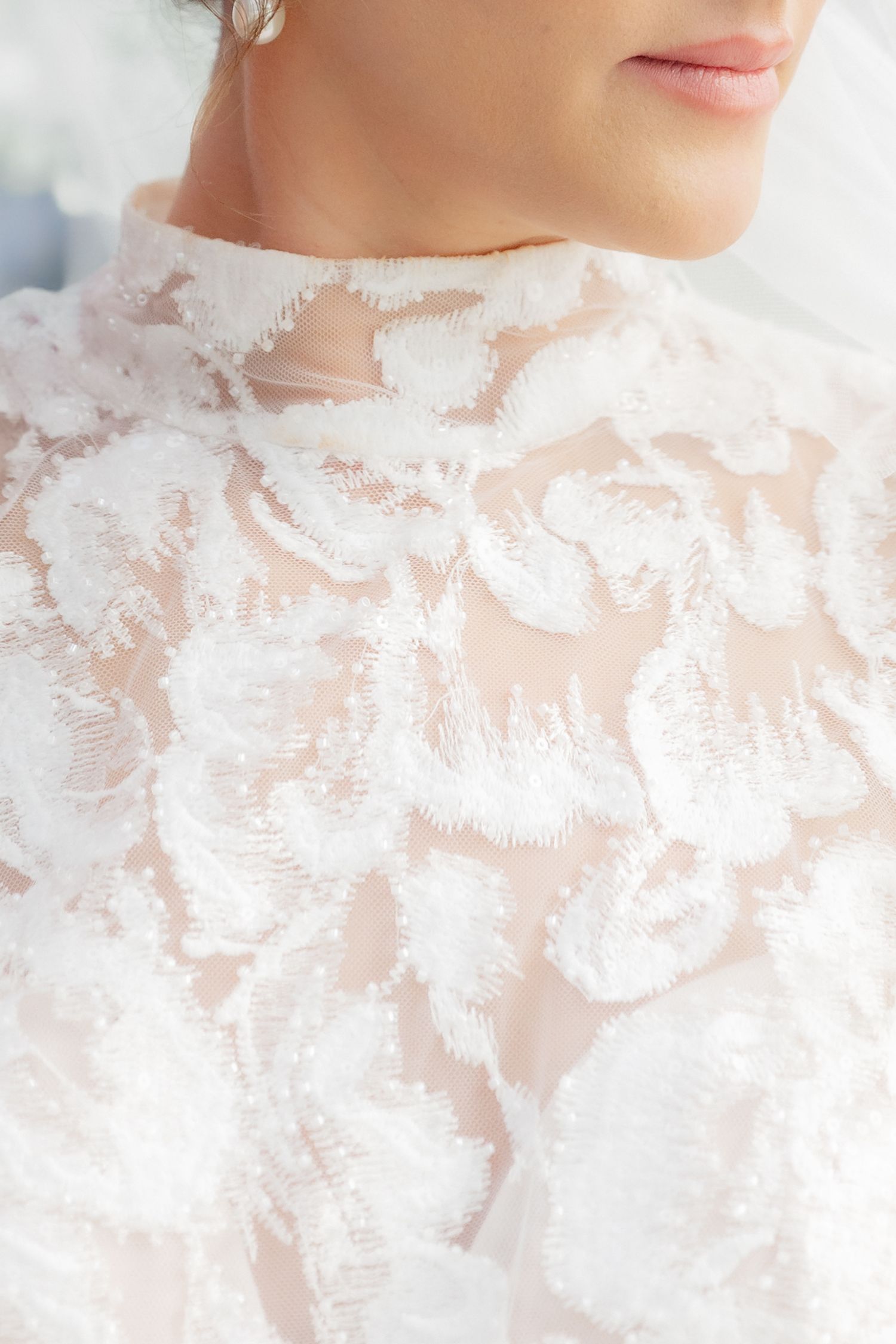 Close-up detail of an intricate white floral lace high-neck wedding dress bodice on a bride.