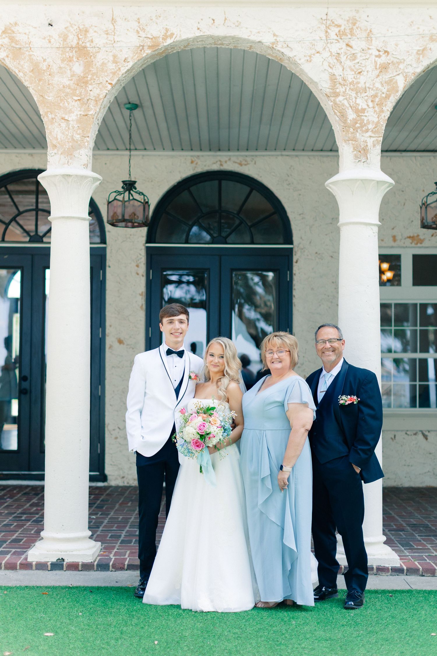 Bride and groom posing with family outside elegant venue with white columns and arched doorways on wedding day, wedding at Bella Cosa