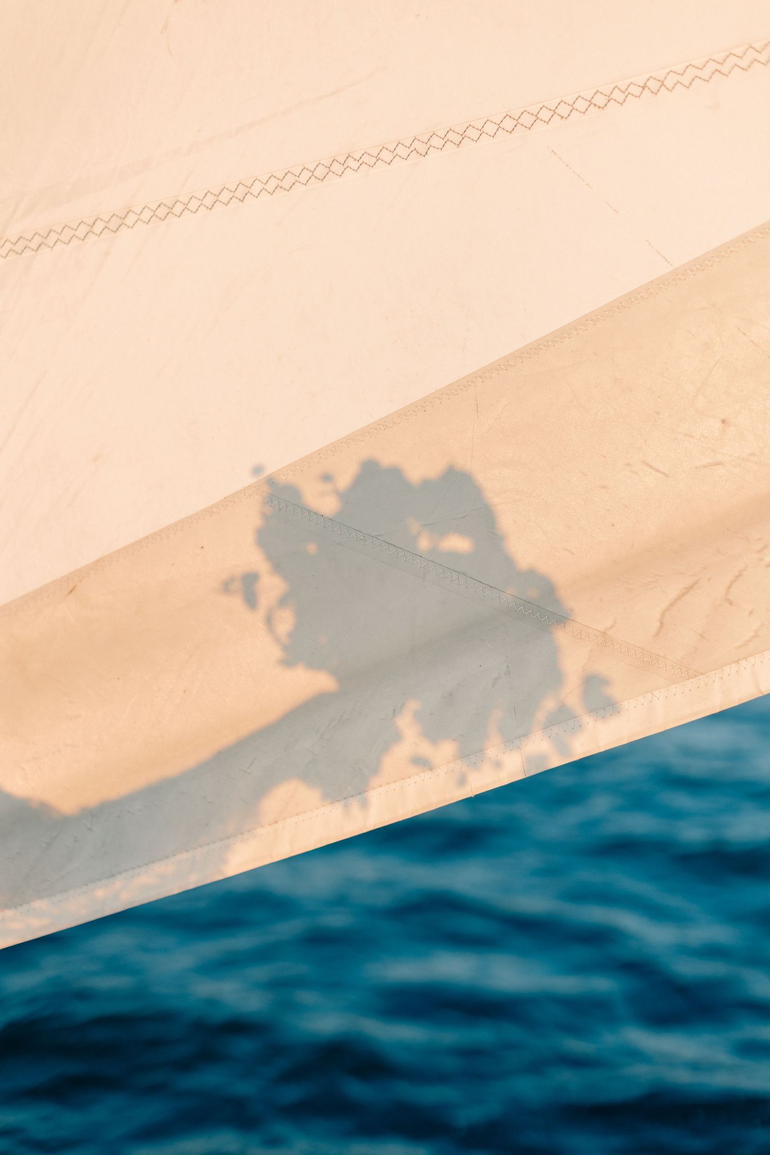 Close-up of a white sail casting a shadow over blue ocean water on a sunny day.