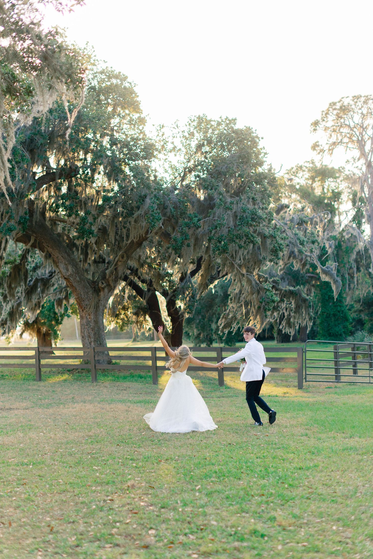 Bride and groom dancing together on lush green lawn surrounded by moss-draped oak trees at outdoor wedding venue, wedding at Bella Cosa