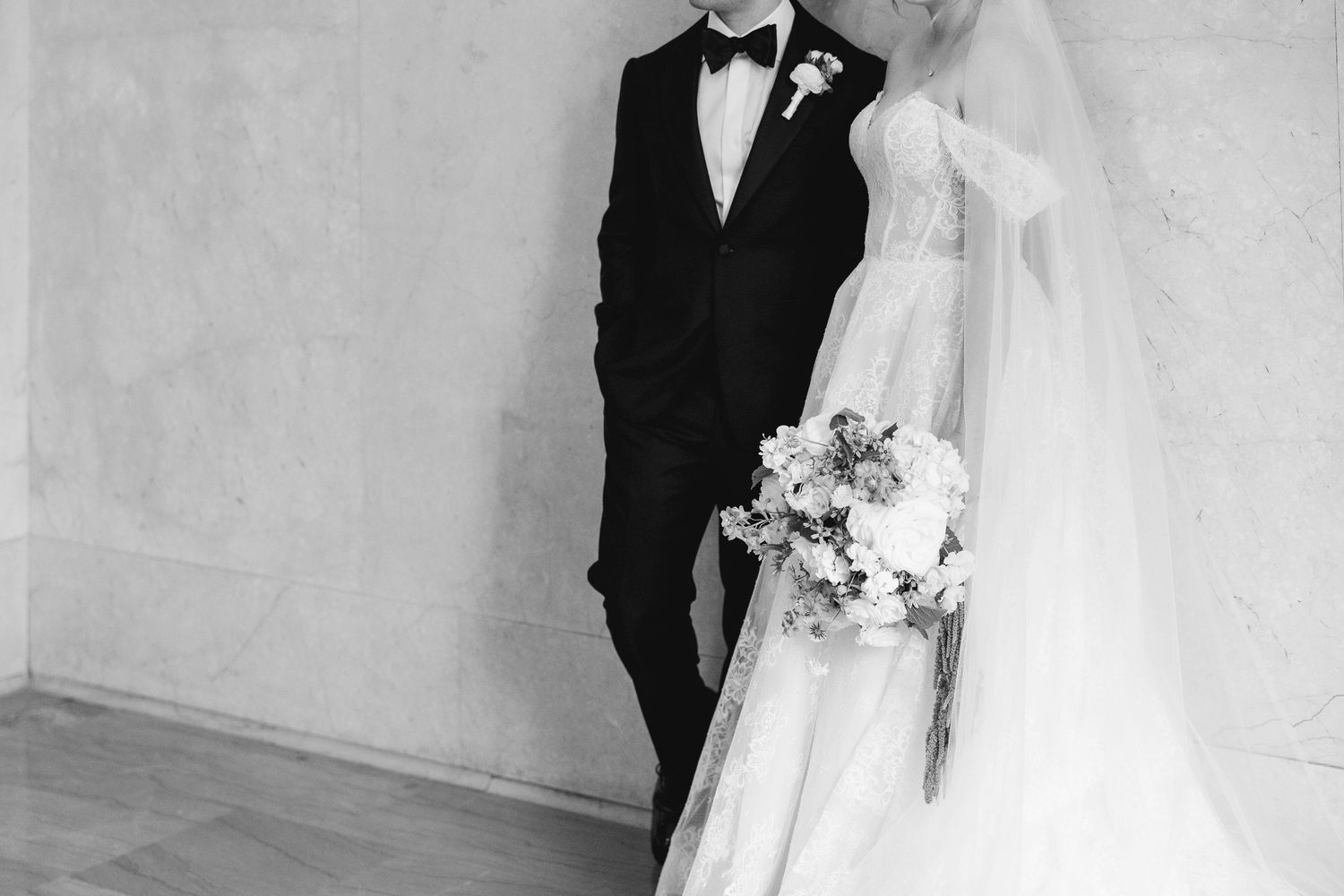 Black and white wedding photo of bride in elegant gown holding bouquet beside groom in classic tuxedo.