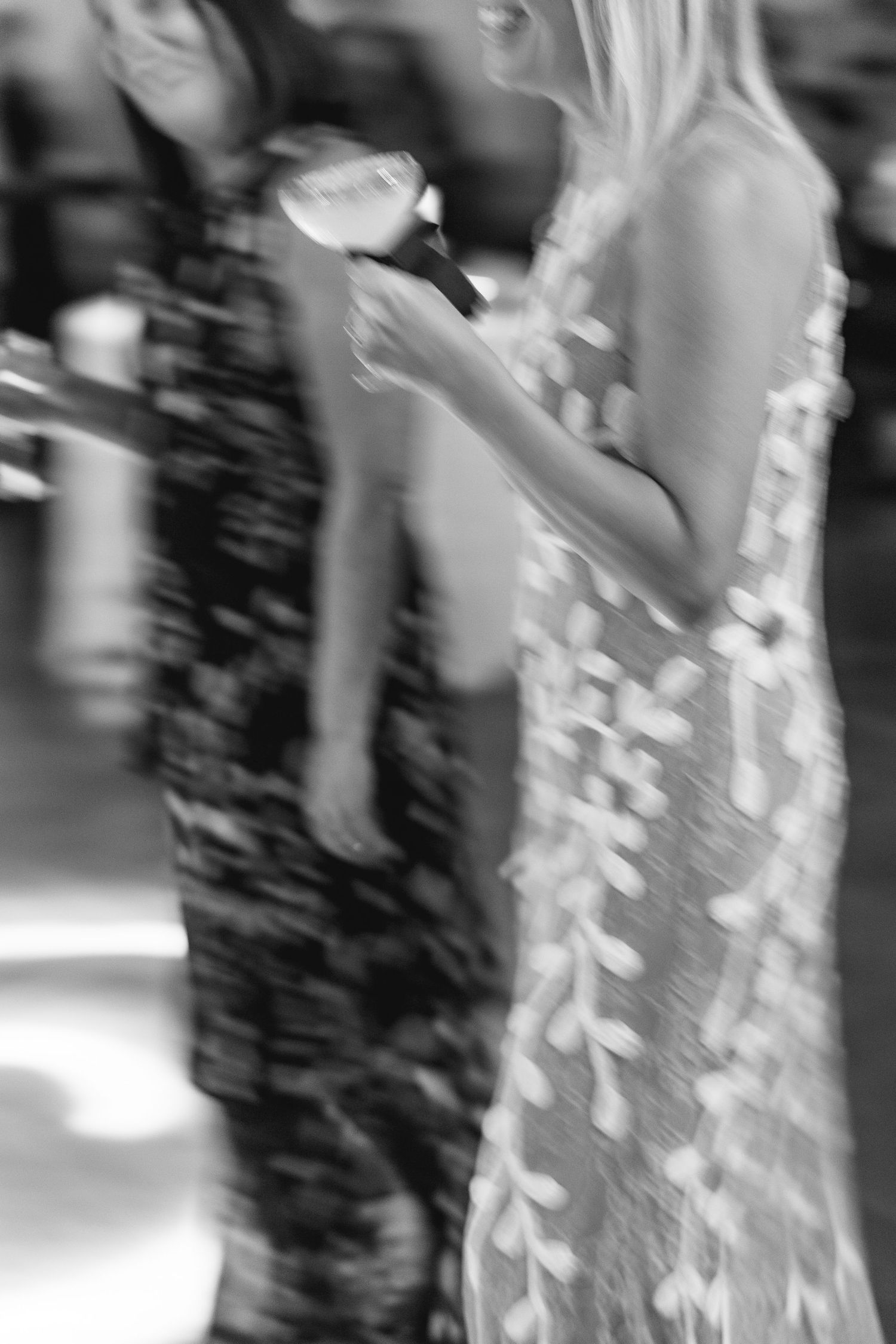 Blurry black and white photo of two women in elegant dresses holding drinks at a formal event.