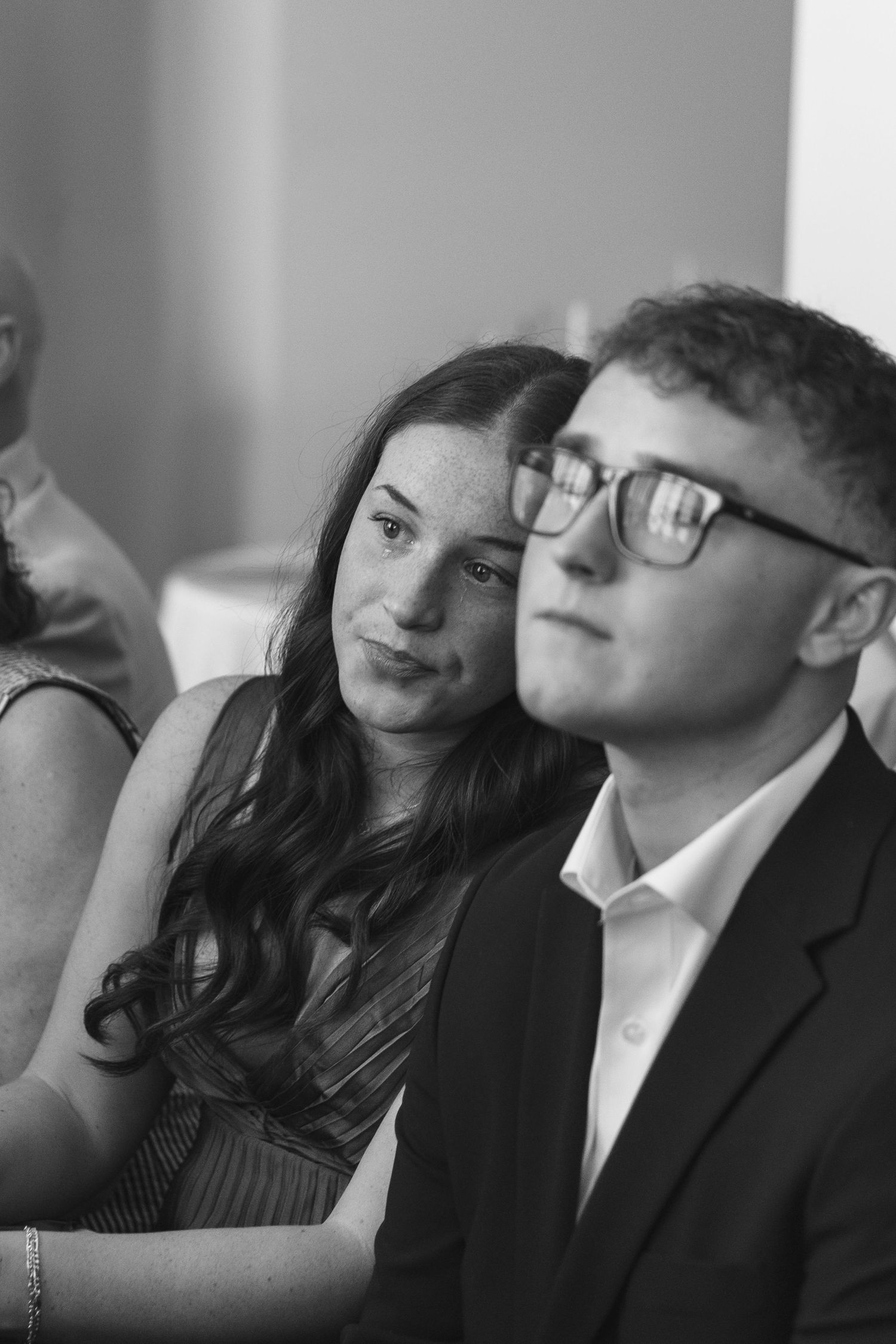 Black and white photo of a young couple at a formal event, woman leaning on mans shoulder, man wearing glasses.