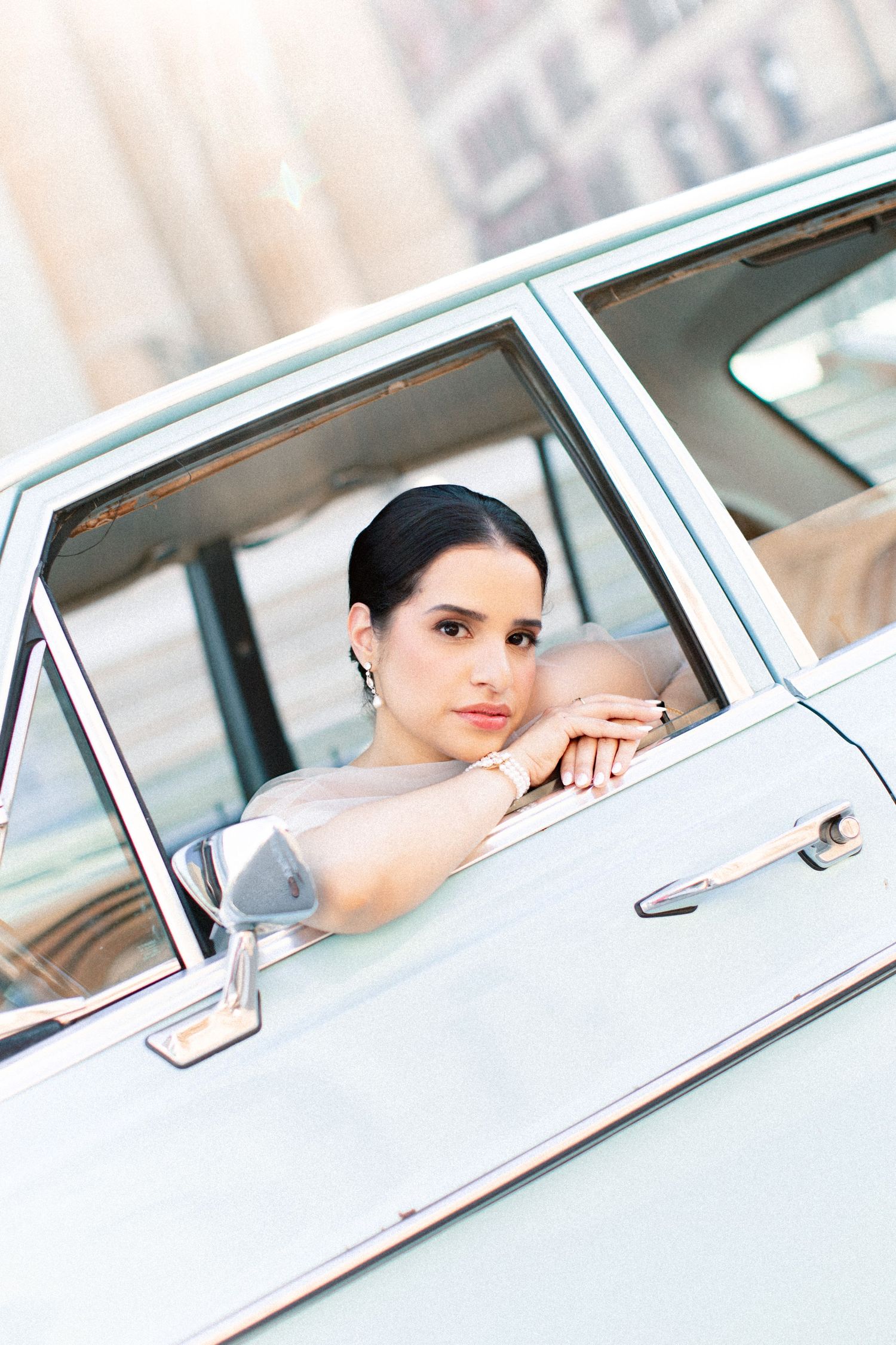 Elegant woman leaning out of a vintage mint green car window, wearing drop earrings and a sheer top.