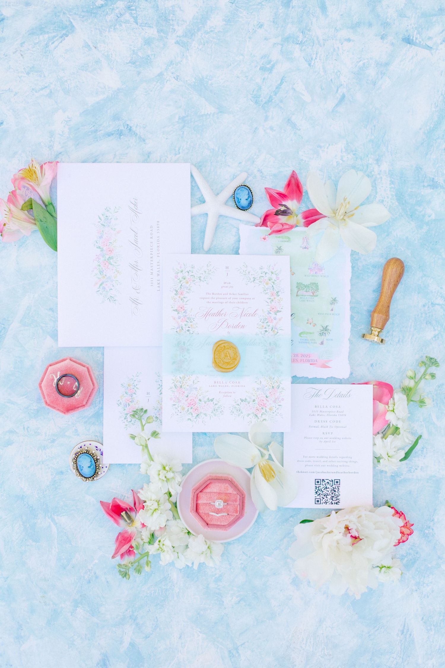 Elegant wedding invitation suite with floral details, gold wax seal, pink ring box, and tropical flowers on blue background, at Bella Cosa