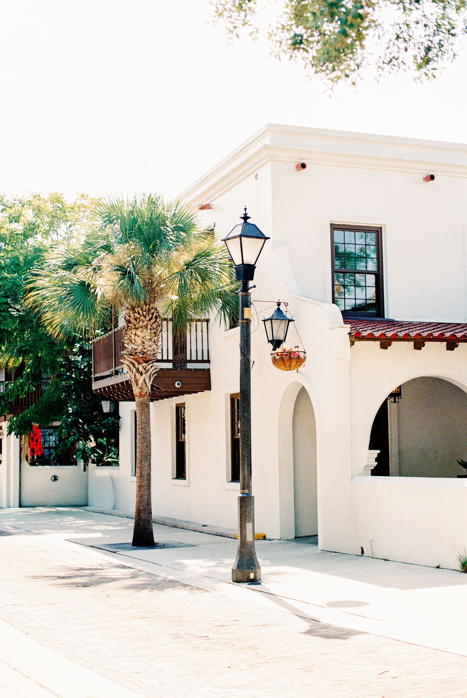 White Spanish-style building with arched doorways, street lamp, and palm tree on a sunny Charleston street corner.