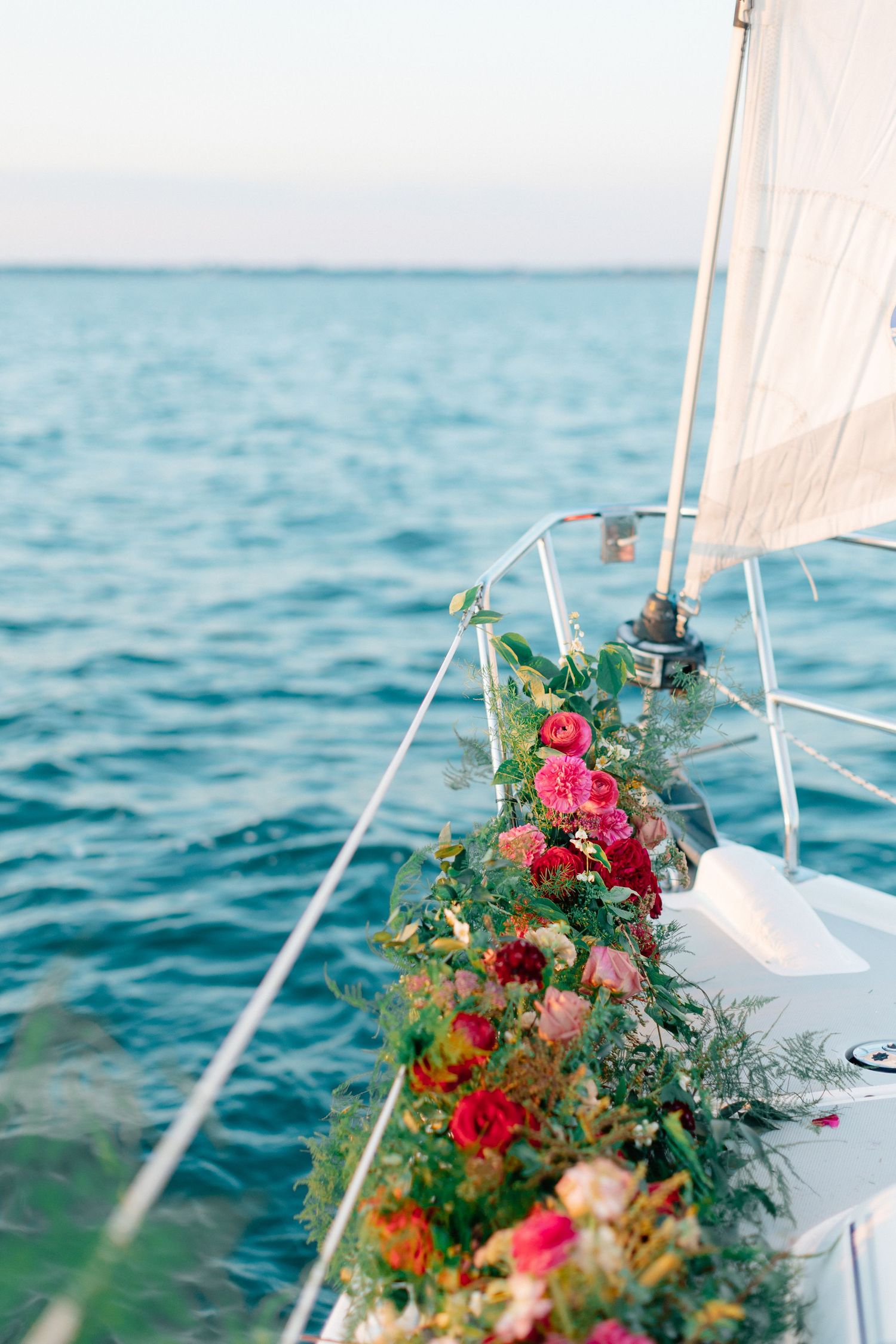 Floral garland of pink and red roses decorating a sailboat railing with turquoise ocean in background.