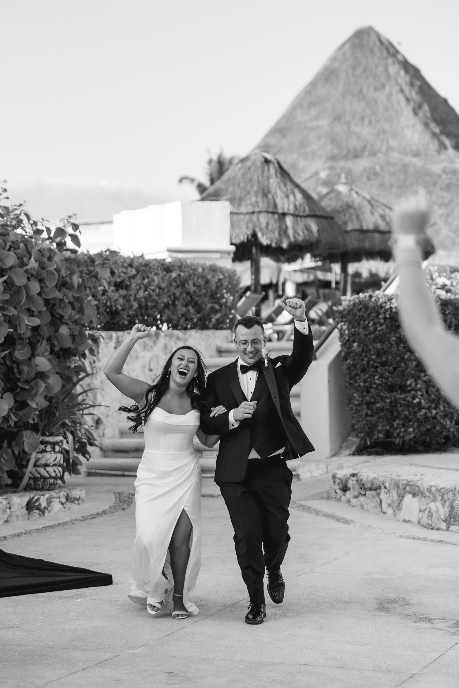 Black and white photo of joyful newlyweds celebrating their grand entrance at a tropical resort wedding venue.