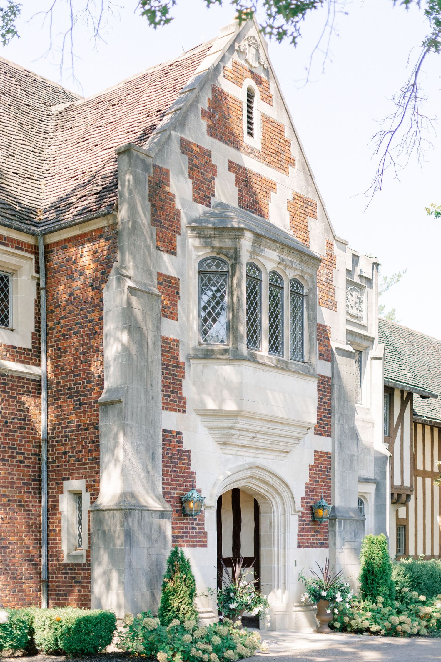 Tudor-style brick wedding venue exterior with arched stone entryway, lattice windows, and lush garden landscaping.