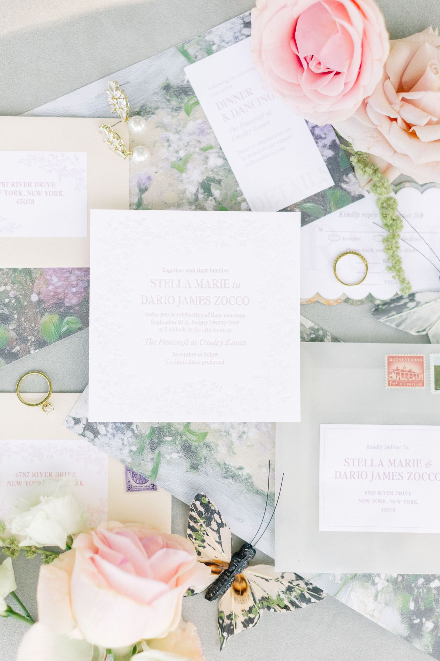 Elegant wedding invitation suite with pink roses, gold rings, butterfly accent, and soft gray envelopes on a romantic flat lay.