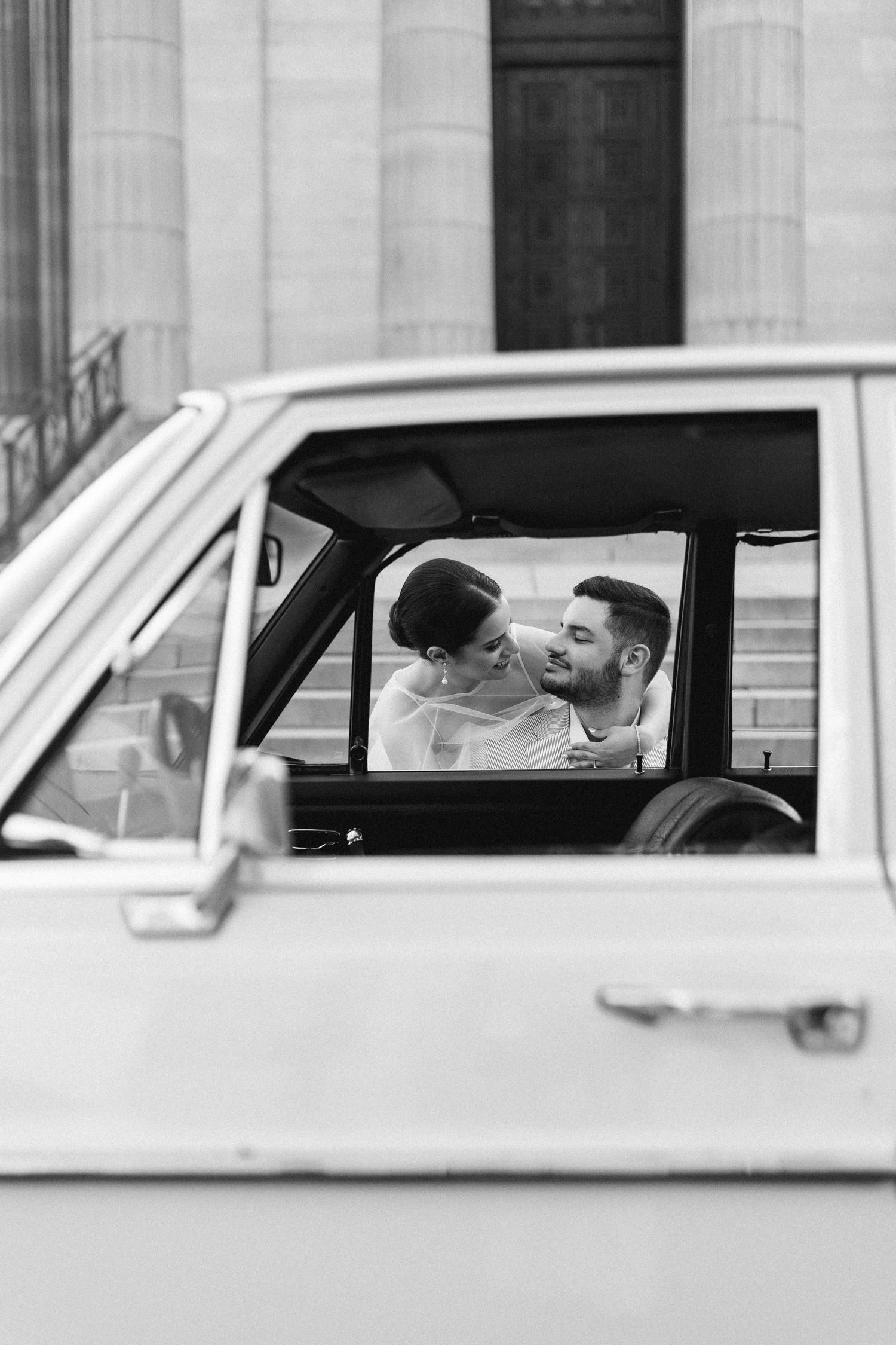 Black and white photo of a romantic couple sharing an intimate moment inside a vintage classic car.